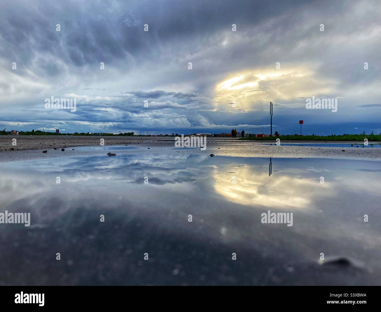 Ein dramatischer Himmel spiegelte sich in einer Pfütze auf dem Tempelhofer Feld, Berlin, Deutschland wider Stockfoto