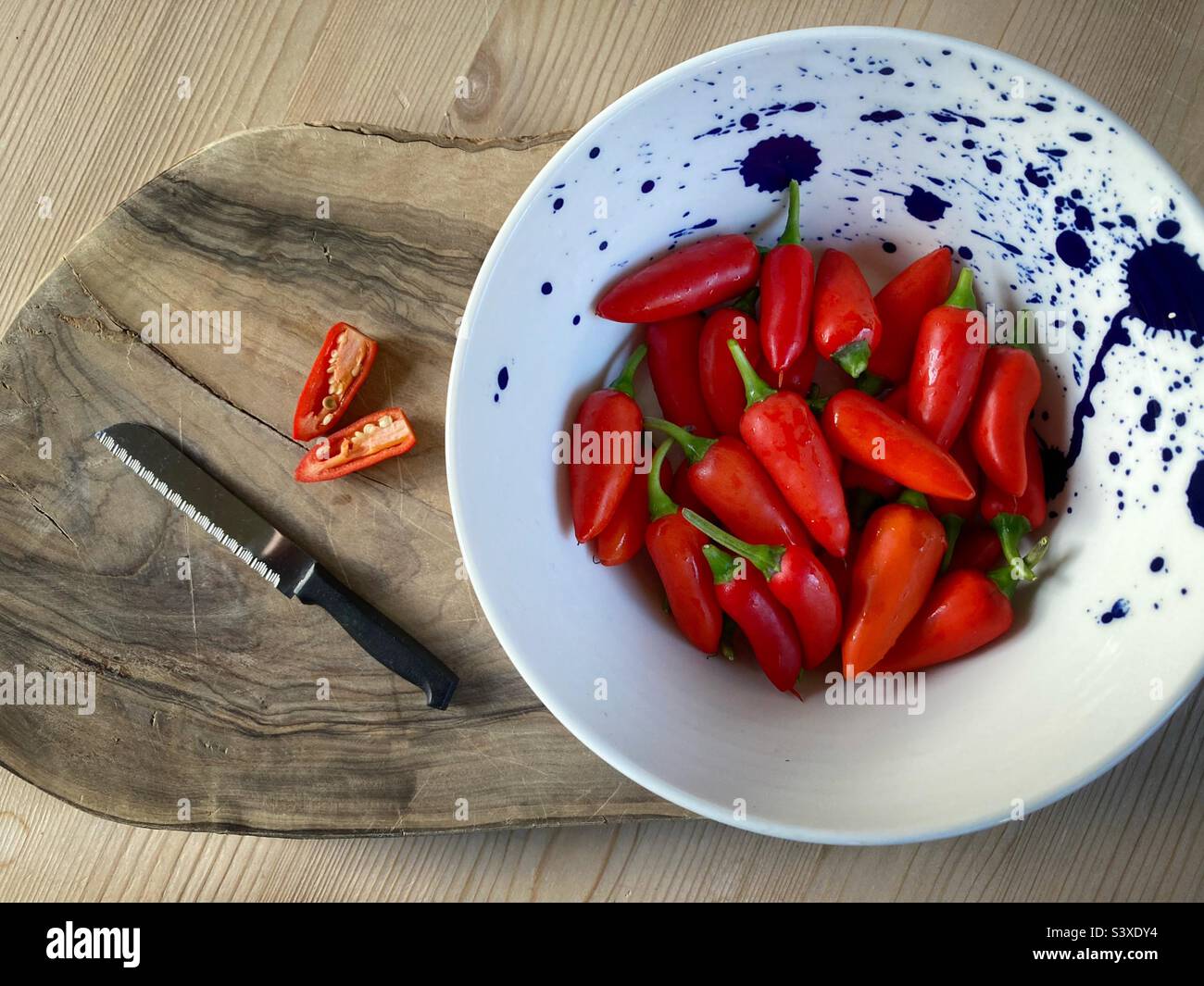 Vorbereiten, um eine rote Chili auf einem Holzbrett mit einer Schüssel Chilis zu hacken Stockfoto