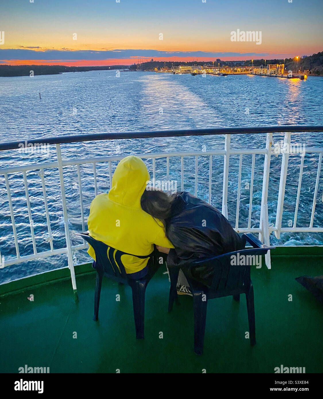 Ein romantisches Paar sitzt zusammen und starrt zurück auf die Insel Åland, während ein baltisches Kreuzschiff den Hafen von Mariehamn im finnischen Sommernachtssonne verlässt - Smartphone-aufgenommenes Stockfoto