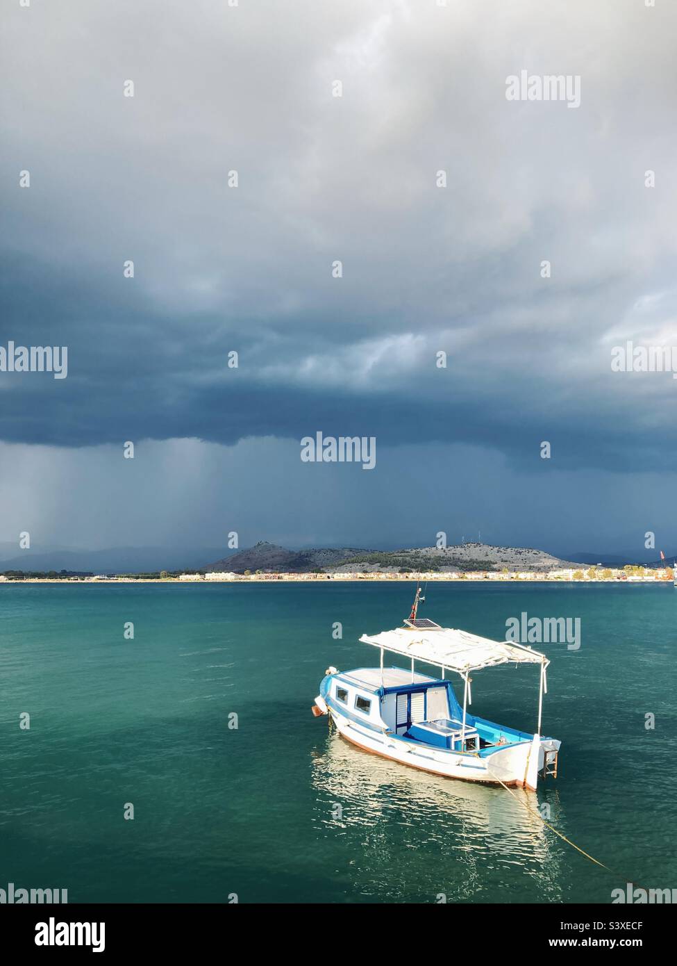Ein Boot in der Sonne im Meer bei Nafplio, Griechenland, mit dunklen stürmischen Wolken am Horizont - Smartphone-aufgenommenes Stockfoto