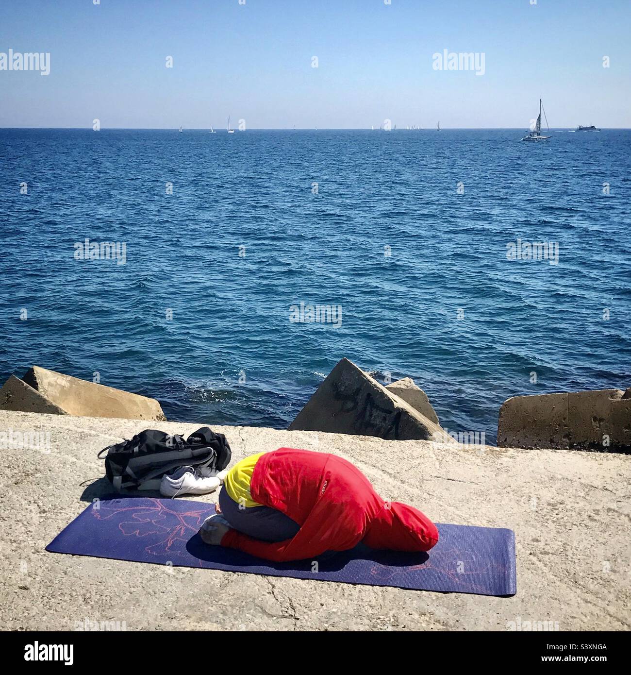 Eine Frau in einem Zen-Moment der Meditation während einer Yoga-Sitzung an der Meereswand vor dem Meer am Strand von Barceloneta in Barcelona, Spanien Stockfoto