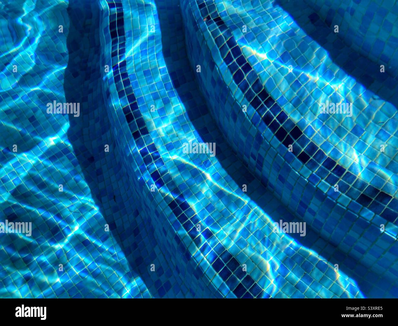 Details zum Swimmingpool, blau geflieste Stufen mit hellen Lichtbrechungen und Wellen. Abstrakter Hintergrund - Smartphone-aufgenommenes Stockfoto