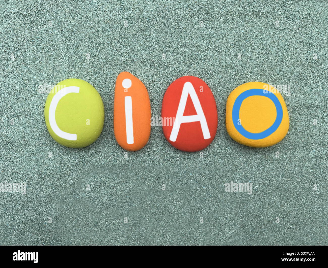 Ciao, italienisches Wort, informeller Gruß, der für Hallo verwendet wird, und Auf Wiedersehen mit farbigen Steinbuchstaben über grünem Sand Stockfoto