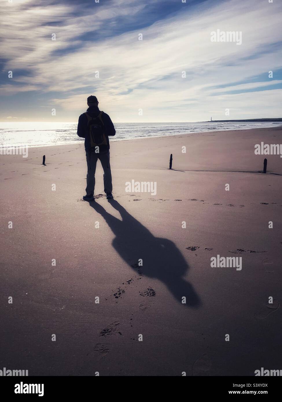 Hinterleuchteter Mann, der bei Ebbe an einem Strand steht Stockfoto