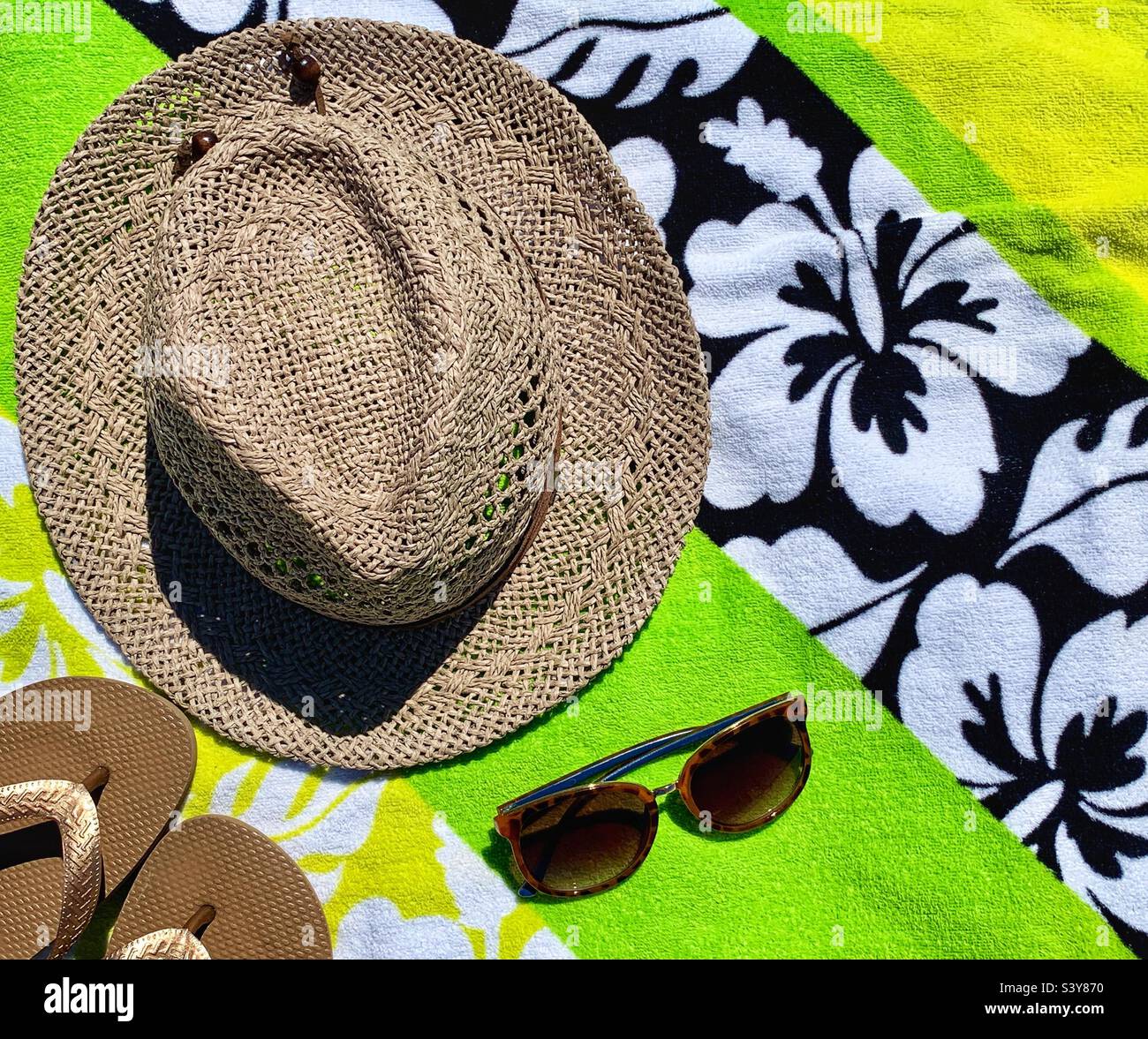 Ein brauner Hut, Sonnenbrille und Hausschuhe auf den Strandhandtüchern - Smartphone-aufgenommenes Stockfoto