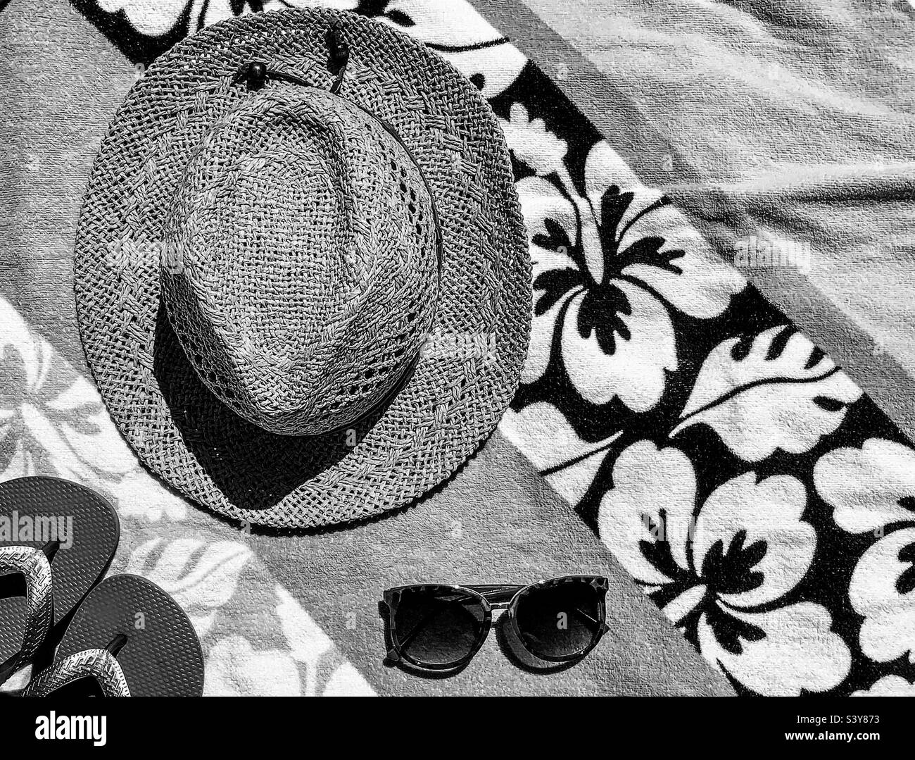 Ein Hut, Sonnenbrille und Hausschuhe auf den Strandtüchern in schwarz-weiß - Smartphone-aufgenommenes Stockfoto