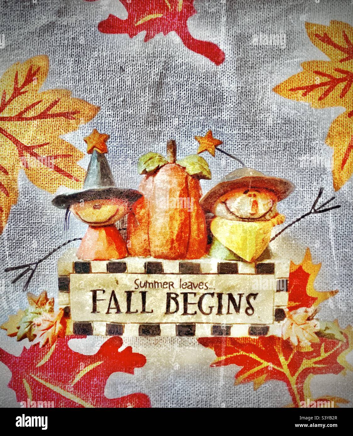Saisonale Wohnkultur auf einem mit Herbstblättern entworfenen Tuch auf einem Wohnzimmertisch. Niedliche herbstliche Vogelscheuchen auf beiden Seiten eines großen Kürbisses, alle sitzen über dem Schild mit der Aufschrift „Sommerblätter fallen beginnt“ Stockfoto
