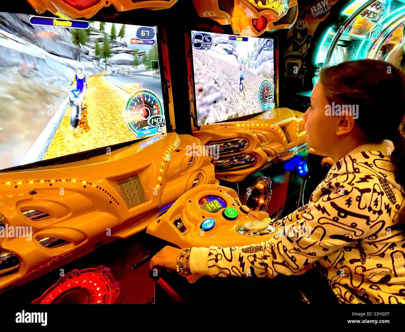 Kleines Mädchen in der Videohalle auf einem virtuellen Motorrad. Stockfoto
