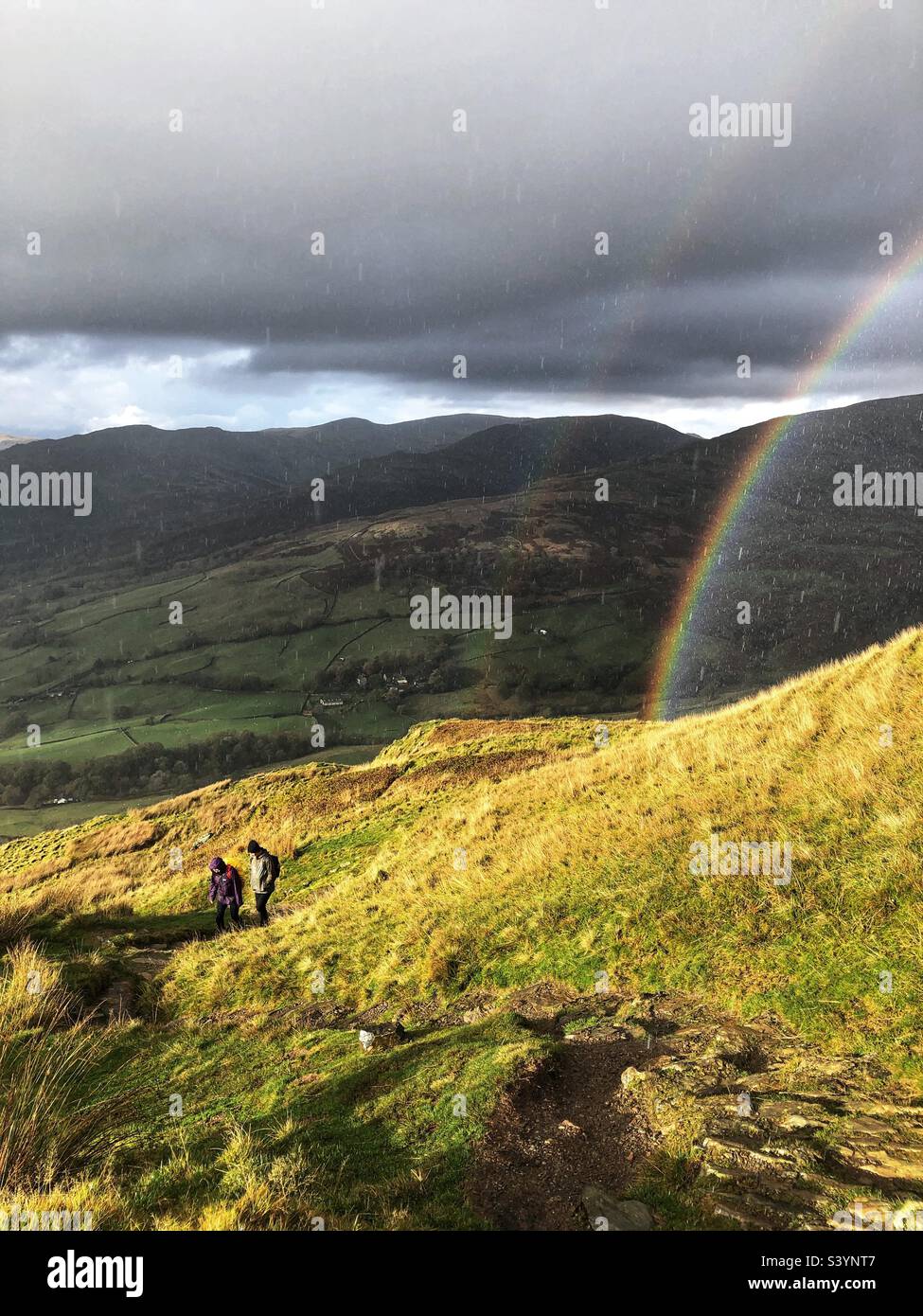 Spaziergänger auf dem Weg zum Wansfell Pike mit Sonne und Duschen und Doppelregenbogen, Ambleside Lake District - Smartphone-aufgenommenes Stockfoto