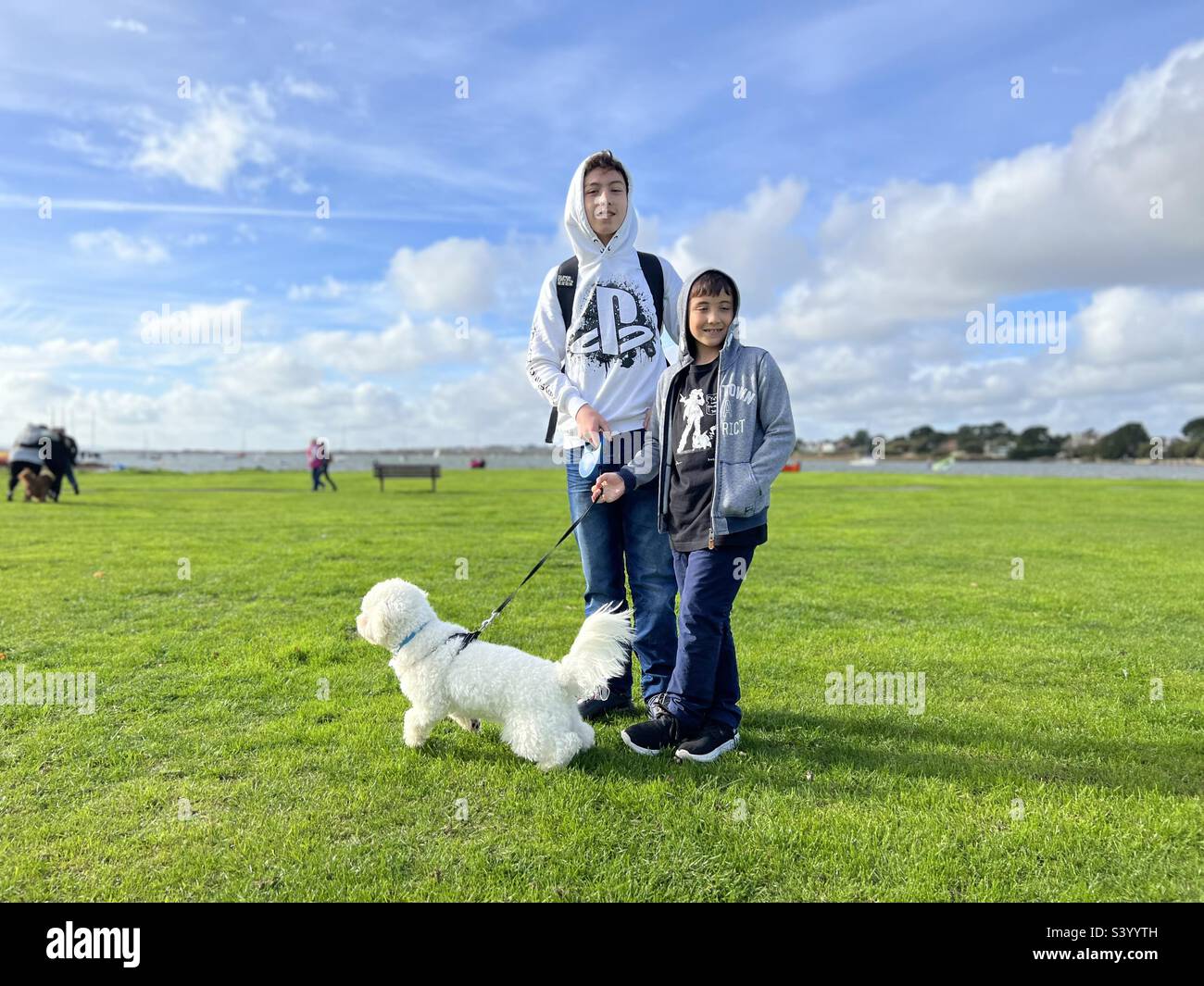 Zwei Jungs posieren für ein Porträt mit ihrem kleinen, weißen Hund Cavapoo. - Smartphone-aufgenommenes Stockfoto