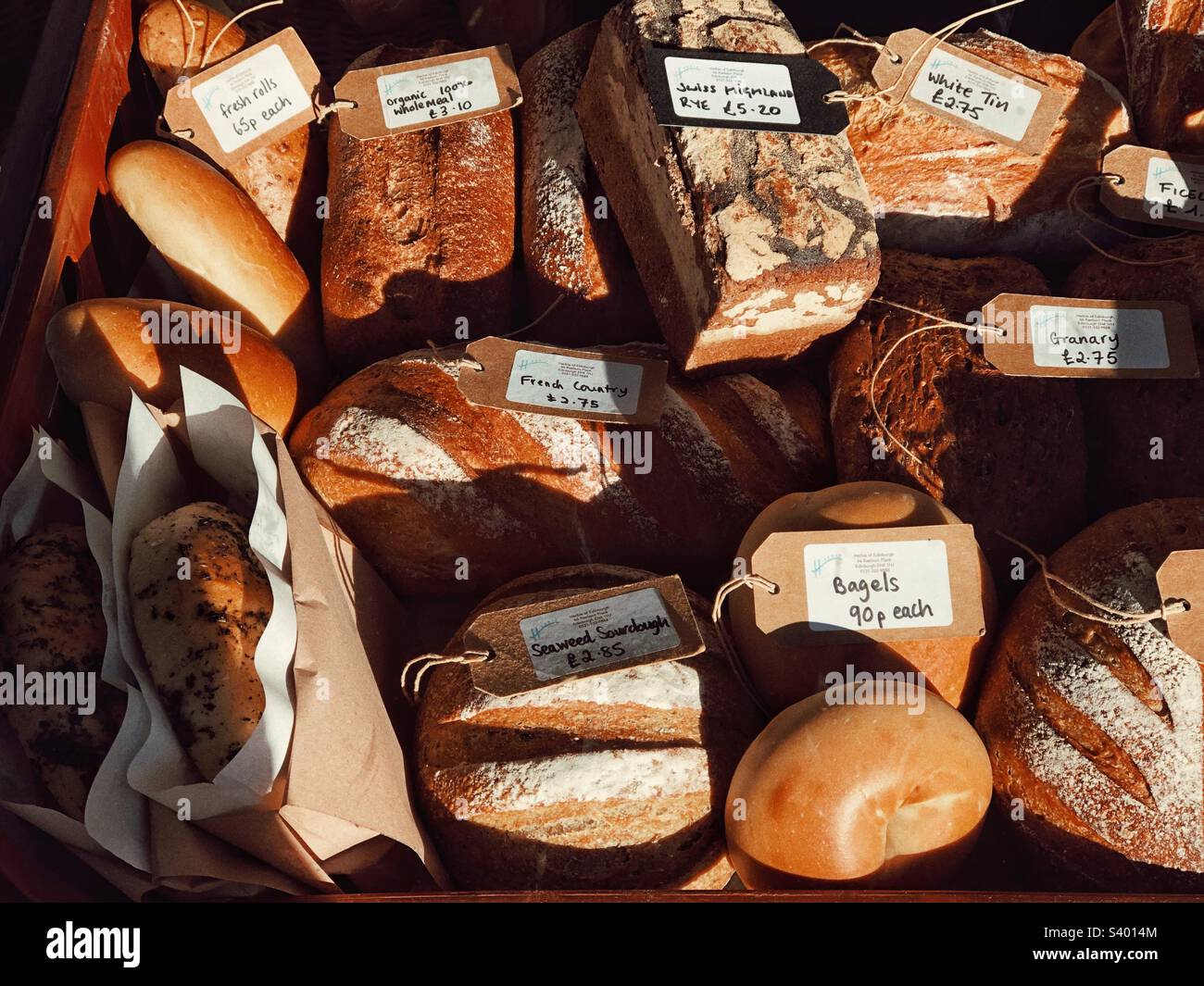 Frische hausgemachte Brotlaibe mit Preisschildern in einem Delikatessengeschäft und einer Schaufensterausstellung für Wurstwaren Stockfoto