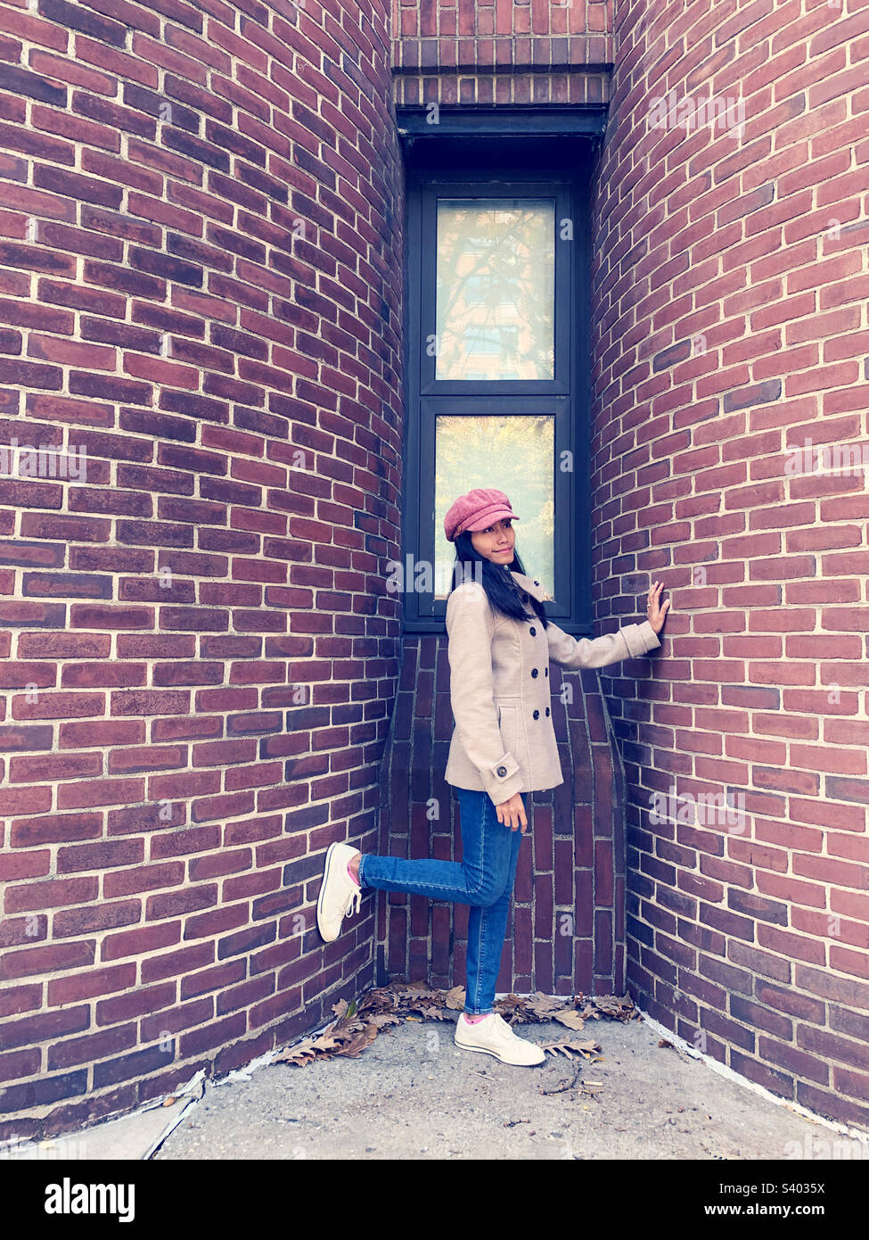 Eine Frau, die gegen die Ziegel von Gebäude 2021 steht - Smartphone-aufgenommenes Stockfoto