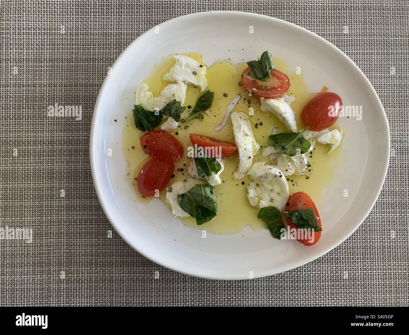Nahaufnahme eines Tomaten- und Mozzarella-Salats garniert mit frischen Basilikumblättern und bespritzt mit nativem Olivenöl Stockfoto