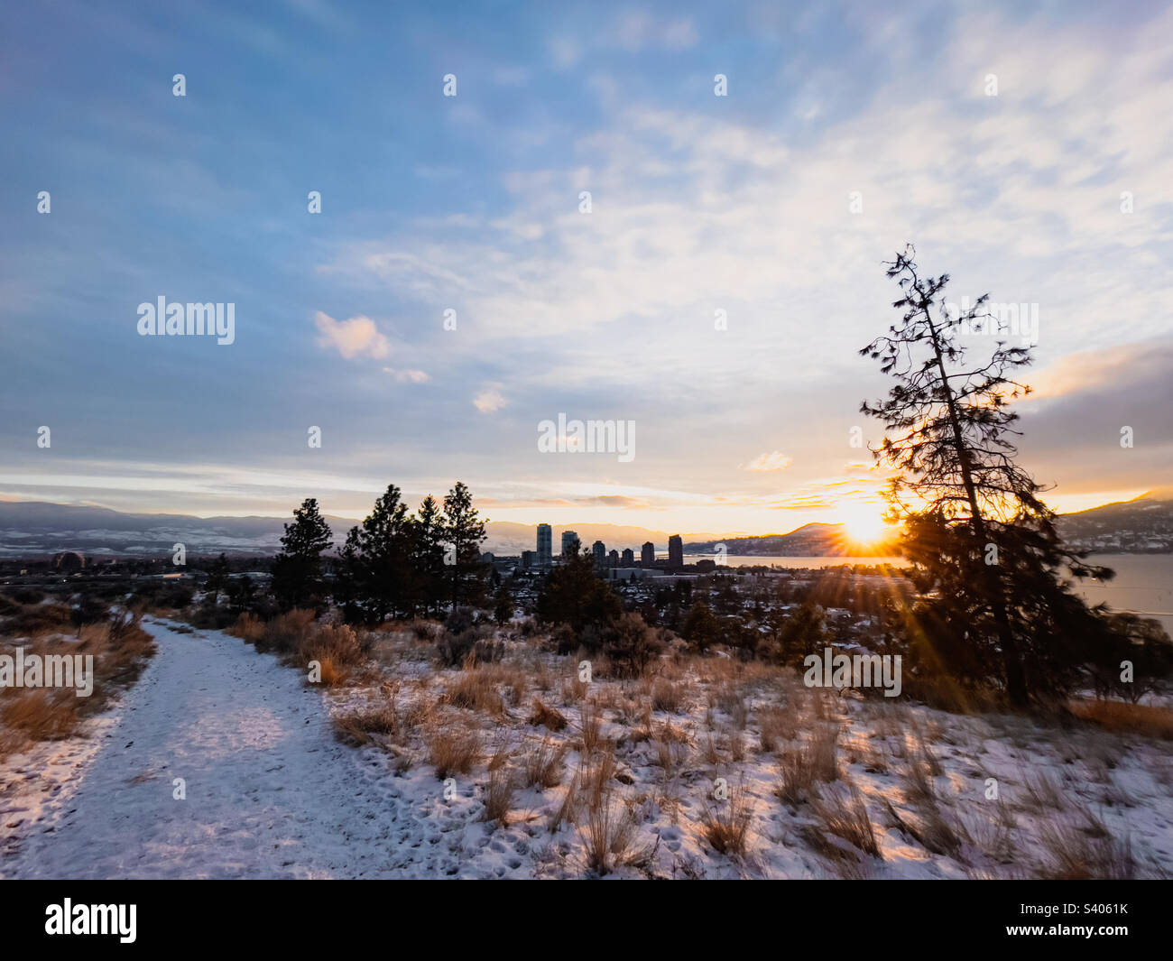 Schneebedeckter Weg auf dem Knox Mountain mit Hochhäusern in der Innenstadt von Kelowna in der Ferne während eines ruhigen Wintersonnenverkehrs. Stockfoto