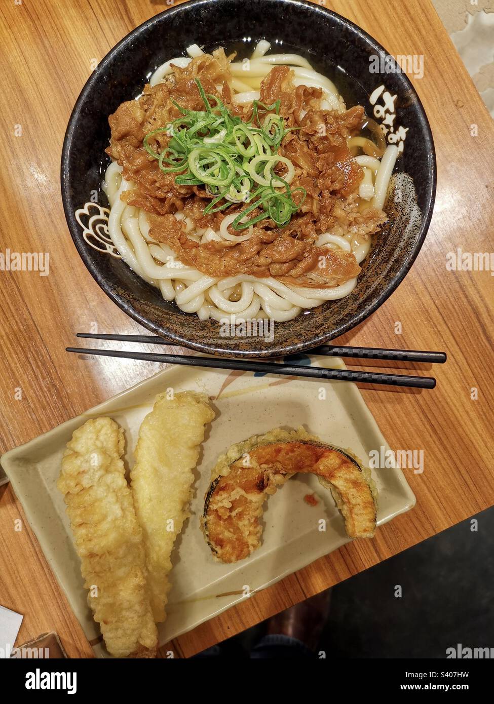 Eine Schüssel Udon-Nudeln und ein Teller Gemüse-Tempura. - Smartphone-aufgenommenes Stockfoto