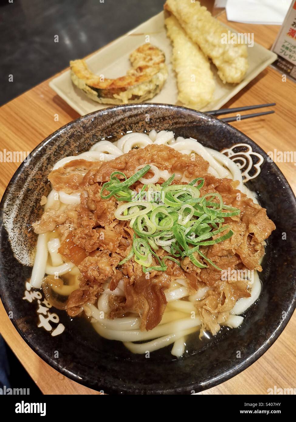 Eine Schüssel Udon-Nudeln und ein Teller Gemüse-Tempura. - Smartphone-aufgenommenes Stockfoto