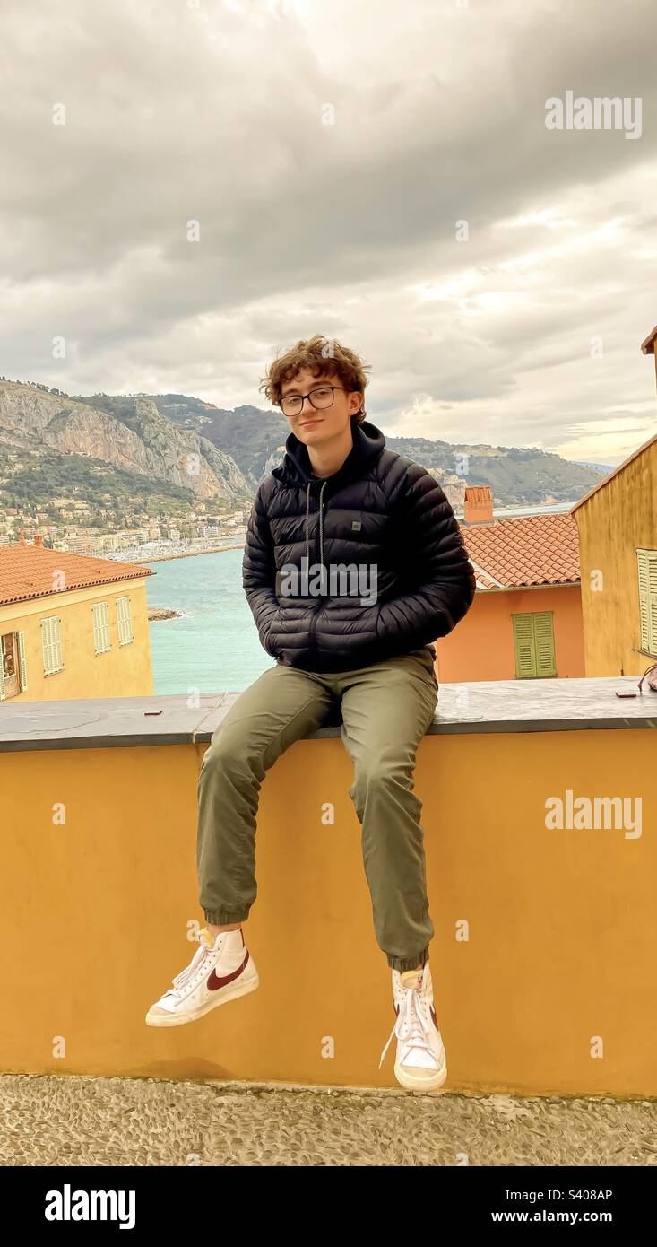 Ein junger Mann posiert für ein Foto auf einem Vorsprung in der französischen Altstadt von Menton. - Smartphone-aufgenommenes Stockfoto