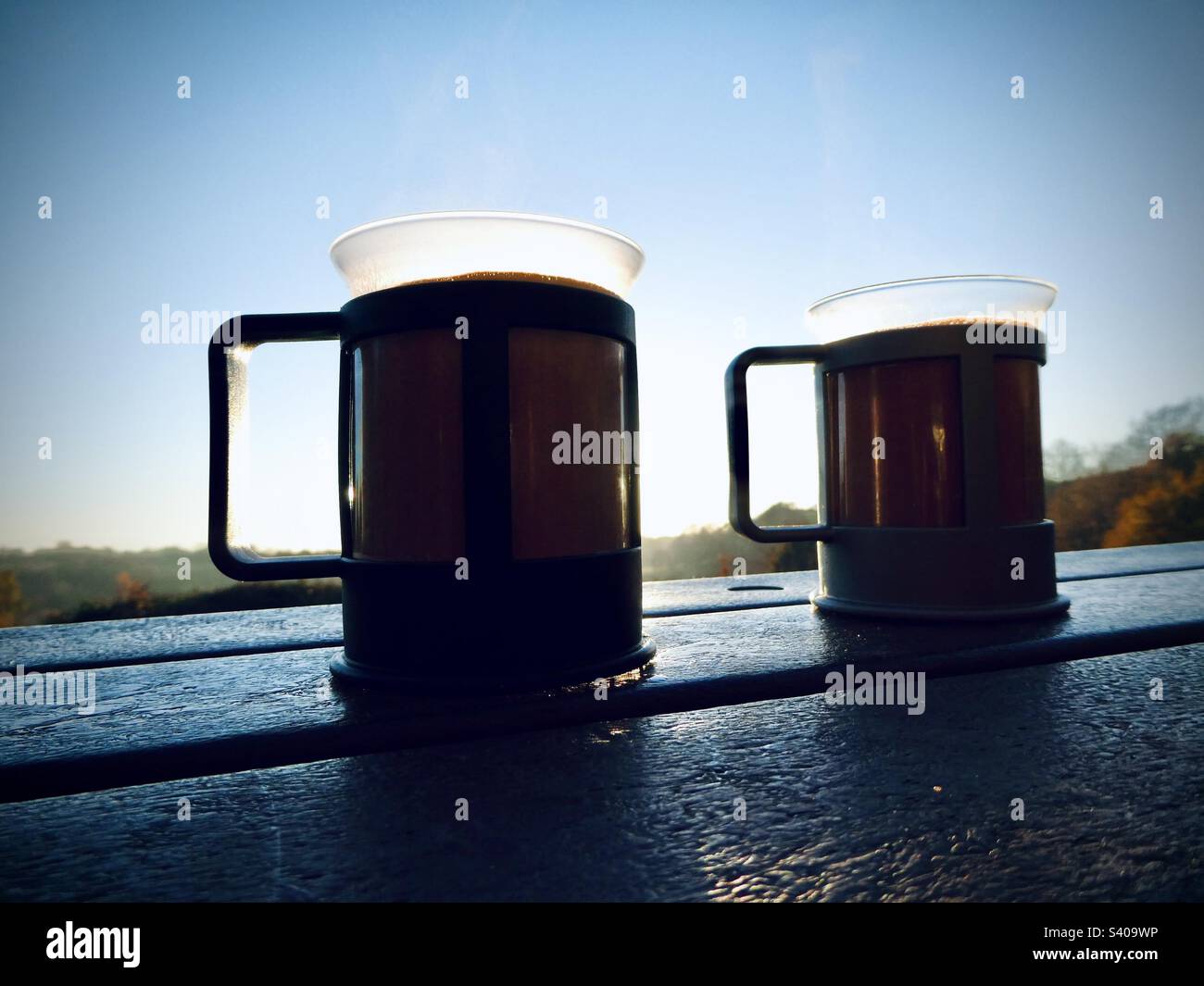 Tassen mit dampfender heißer Schokolade liegen an einem kalten Tag in England in Großbritannien auf einer Parkbank Stockfoto