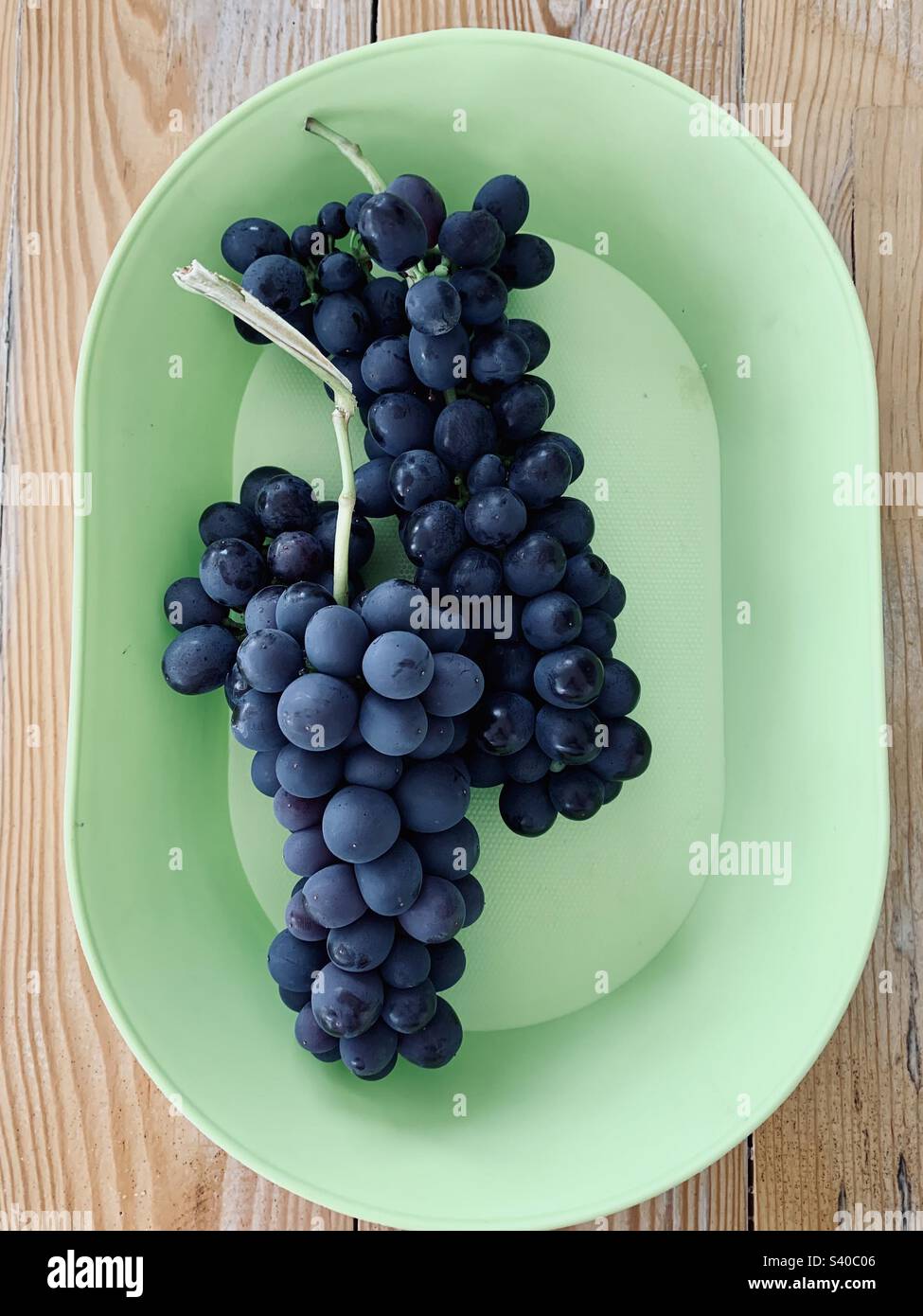 Rote Trauben in einer grünen Schüssel auf einem Holztisch - Smartphone-aufgenommenes Stockfoto