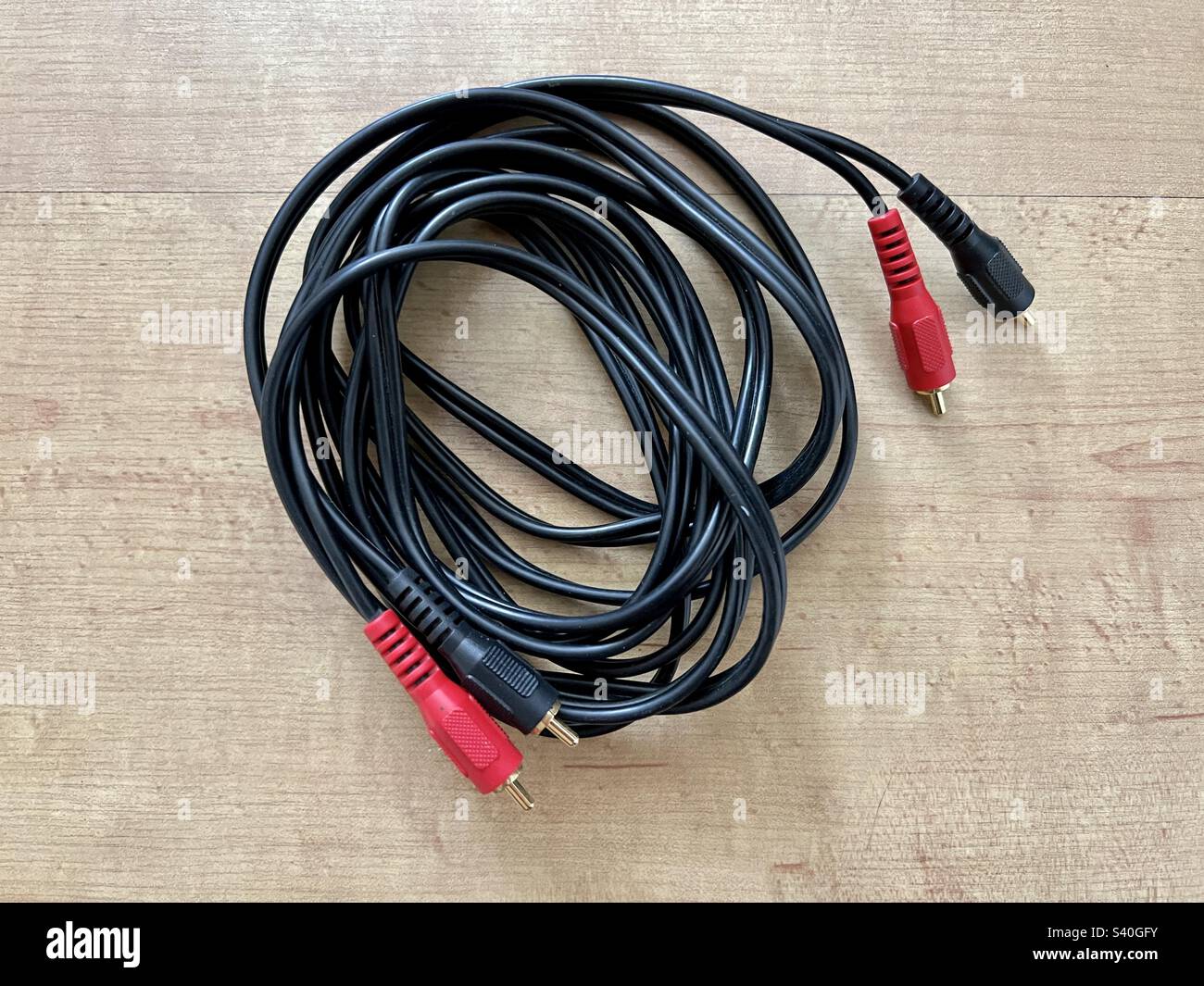 Schwarzes Stereo-Audiokabel mit roten und schwarzen Kunststoffabdeckungen über vergoldeten Cinch-Anschlüssen an beiden Enden auf glatter Holzoberfläche - Smartphone-aufgenommenes Stockfoto