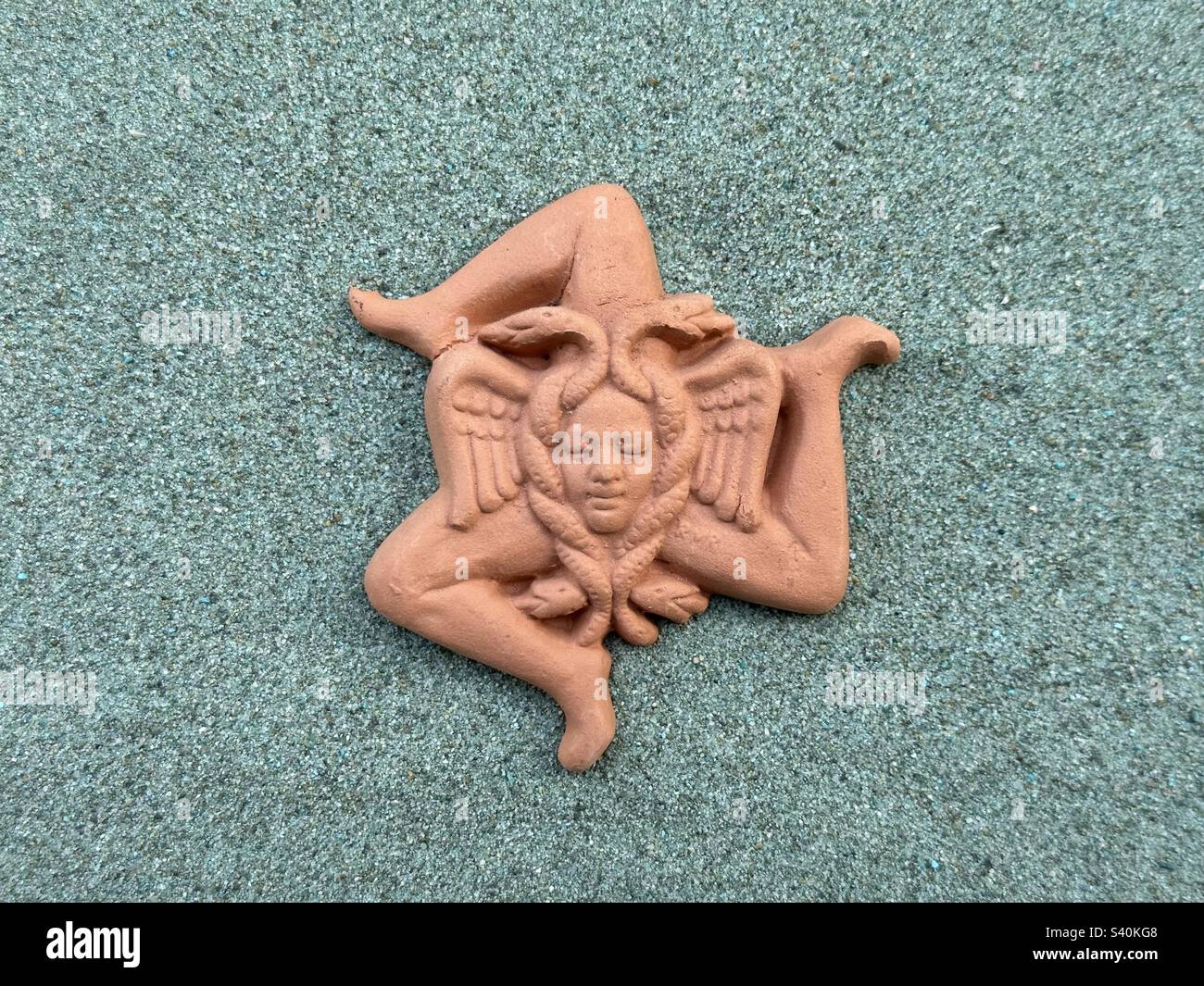 Terrakotta handgemachtes Trinacria-Symbol, weltweit bekannt als das Emblem von Sizilien über grünem Sand Stockfoto