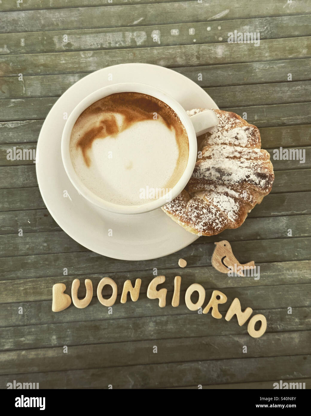 Buongiorno, italienischer Good Morning Text mit handgefertigten hölzernen Buchstaben vorne an einem Cappuccino mit Croissant Stockfoto
