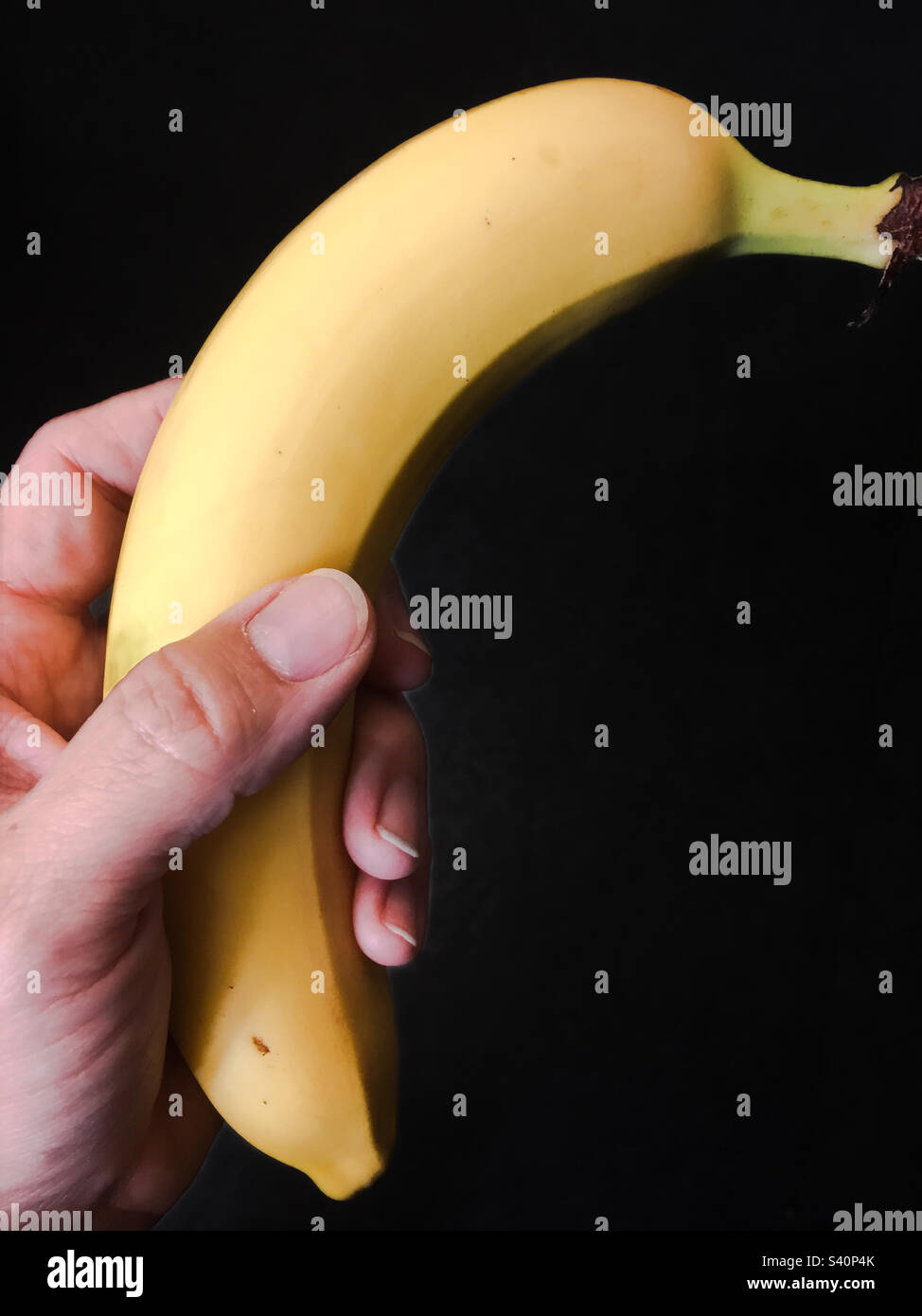 Hand mit einer Banane mit schwarzem Hintergrund - Smartphone-aufgenommenes Stockfoto