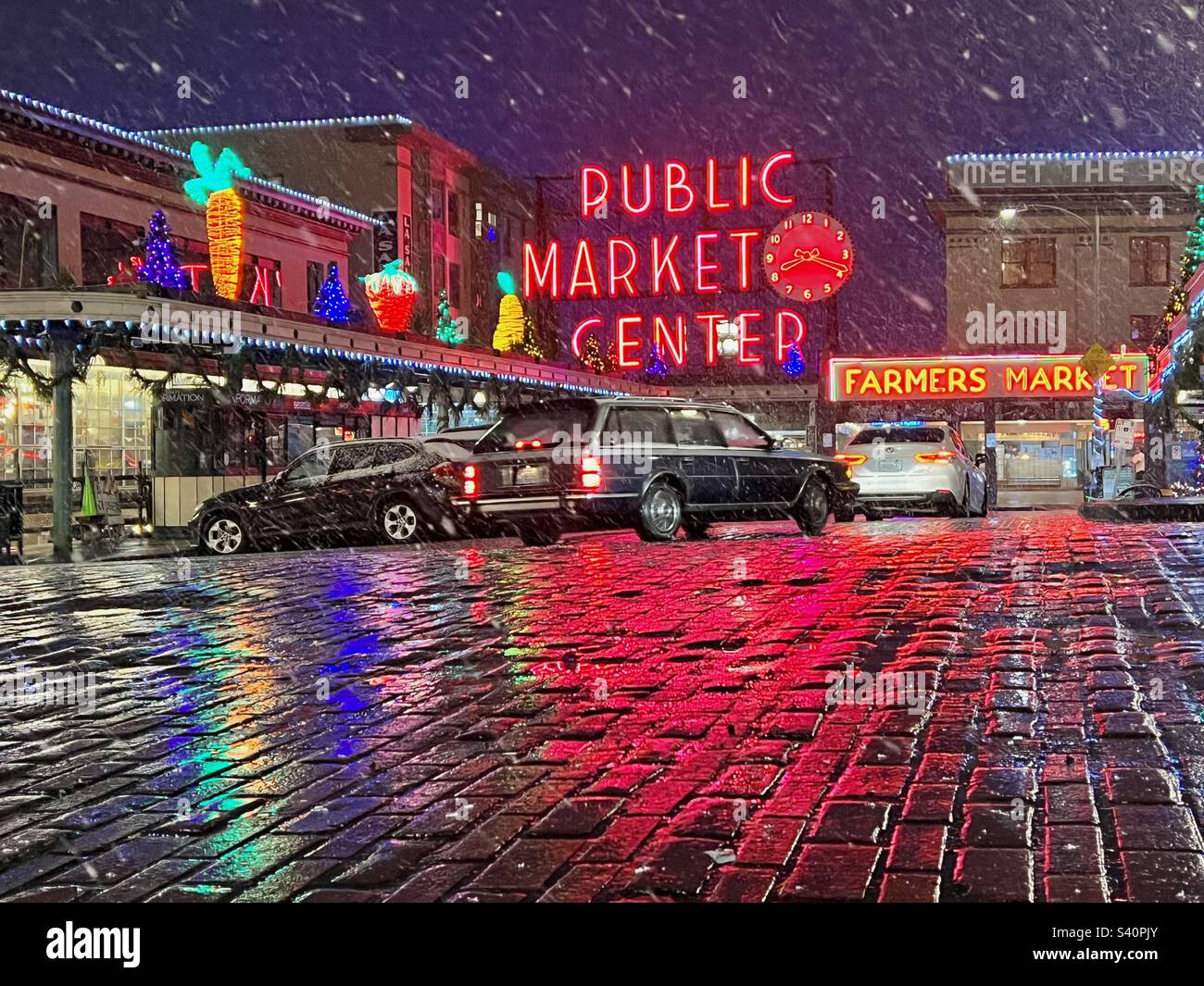 Der Pike Place Market im Zentrum von Seattle, USA, im nächtlichen Schneesturm mit bunten Neonlichtern auf nassen Ziegelsteinstraßen. - Smartphone-aufgenommenes Stockfoto