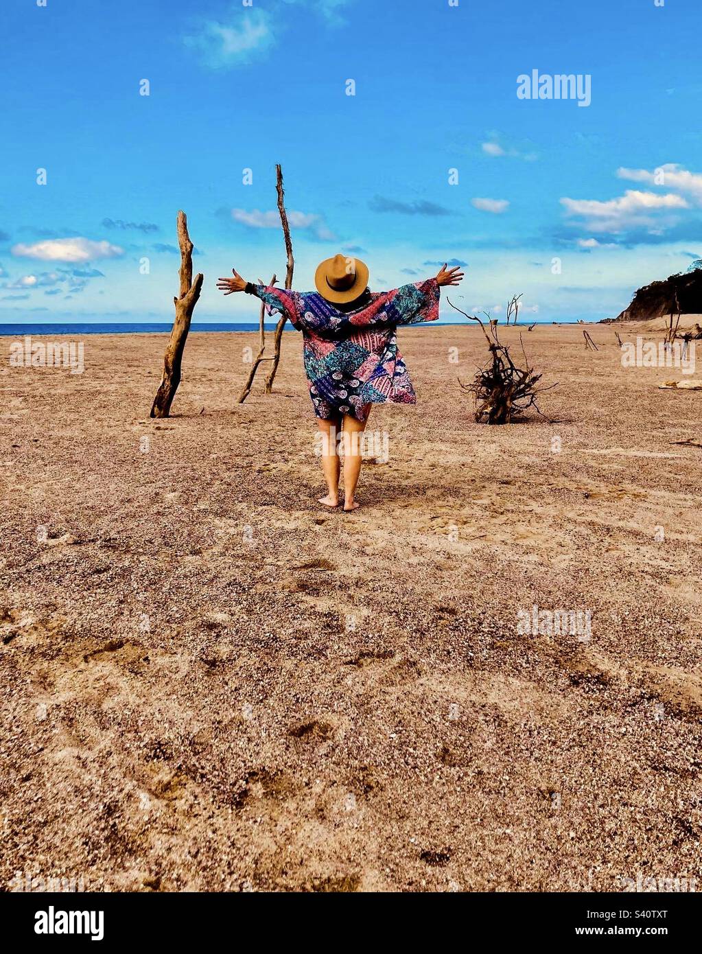 Eine Frau mit ausgestreckten Armen nimmt die erstaunliche Natur des Lo De Marcos Strandes auf. Stockfoto