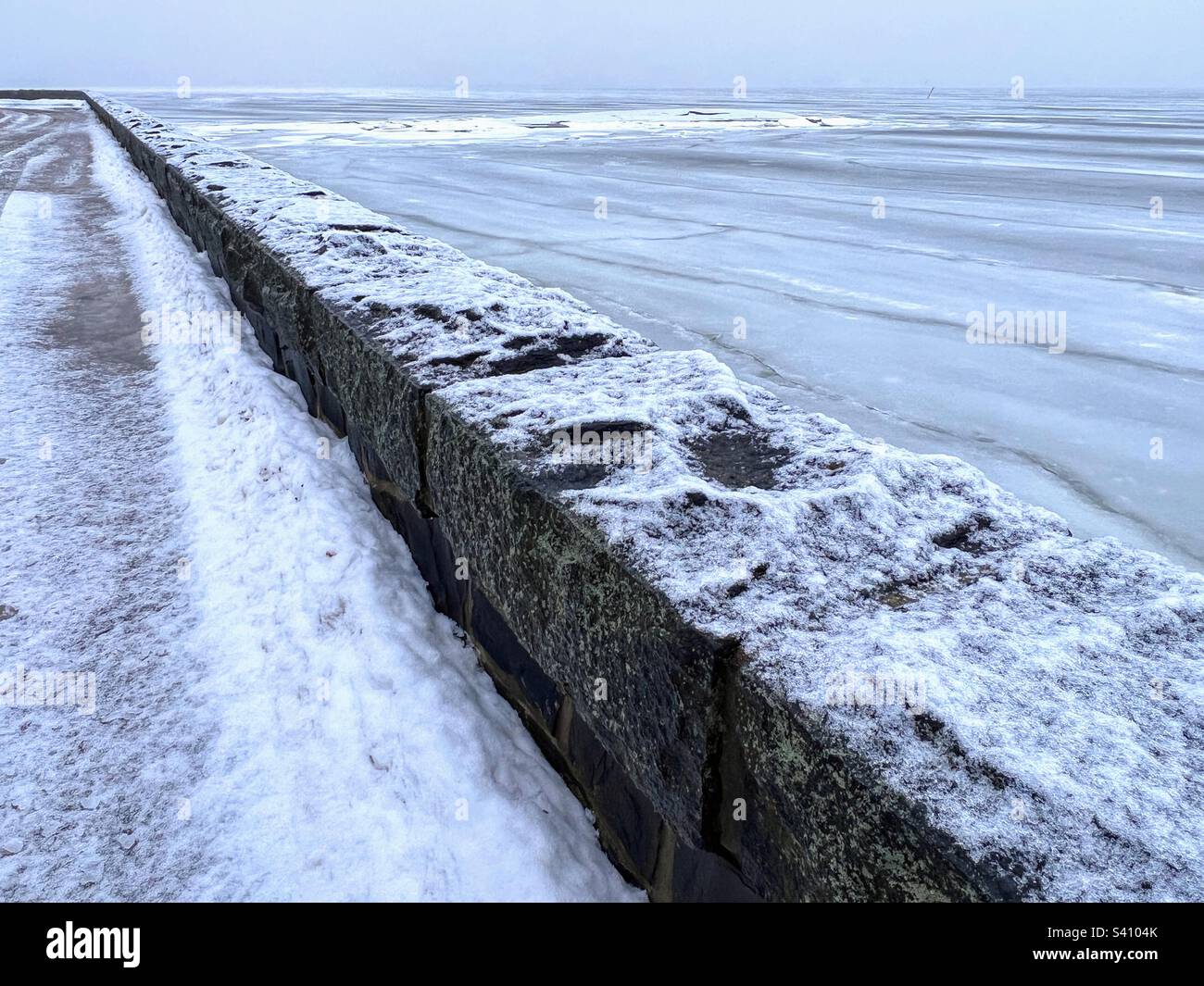 Im Winter schneebedeckte Aussicht über den niedrigen Steinzaun auf die eisige Ostsee mit Eisschollen Stockfoto
