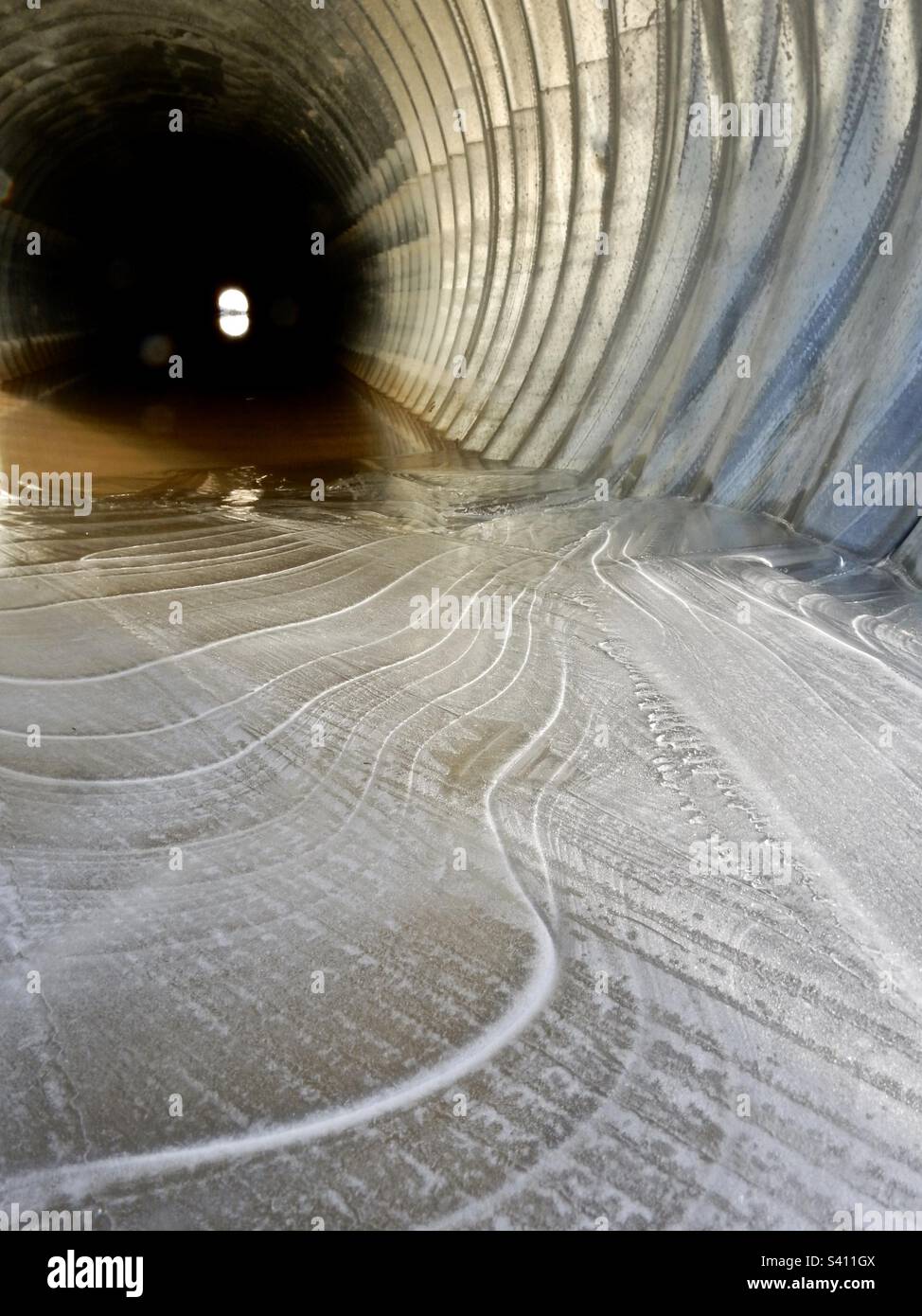 Eisformationen auf einer Pfütze in einem Kanal. Yukon. Die Linien und Strukturen bilden sich über Nacht und schmelzen tagsüber. Sie können auch das andere Ende des Auslasses sehen. - Smartphone-aufgenommenes Stockfoto