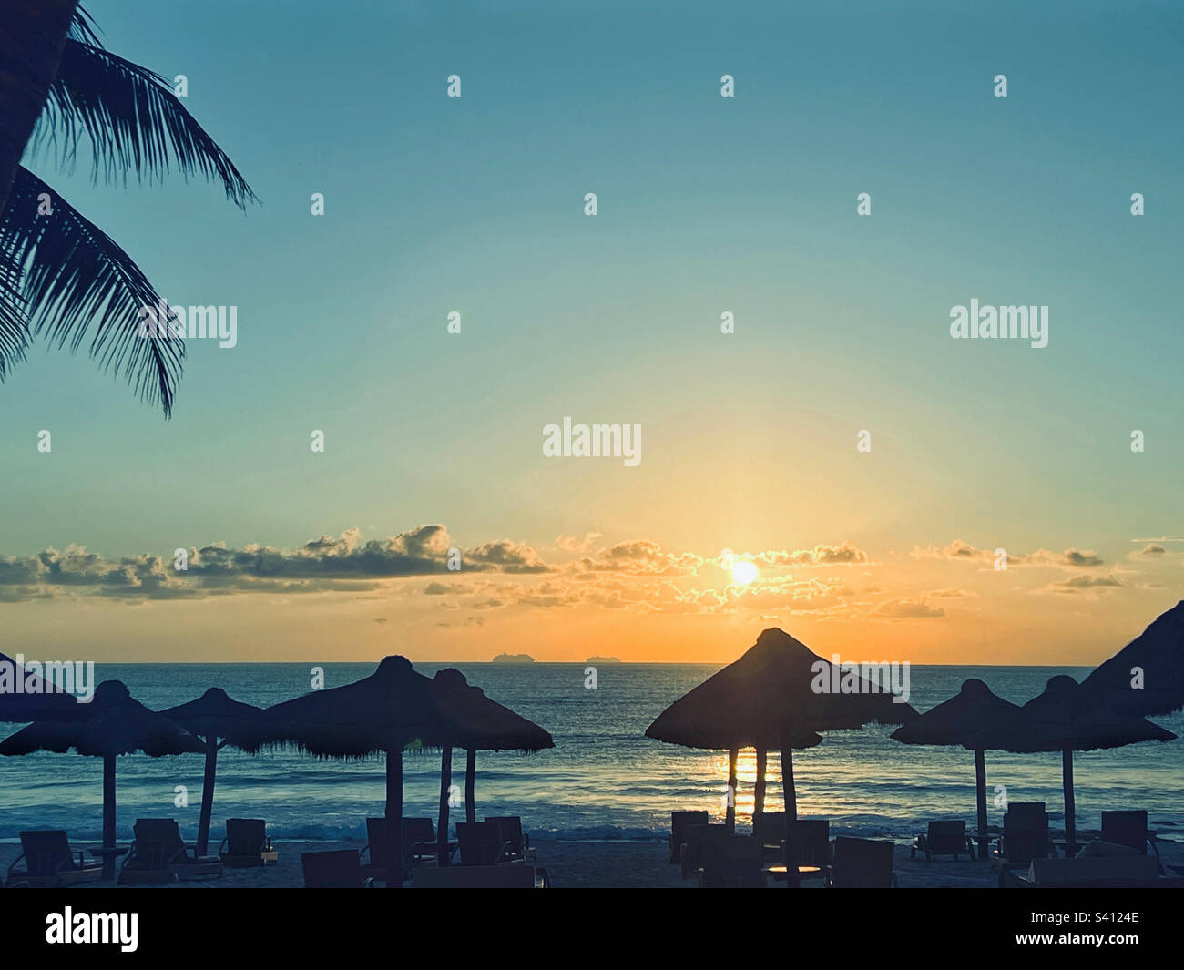 Liegestühle und Palapas vor dem Karibischen Meer in Mexiko bei Sonnenaufgang. Stockfoto