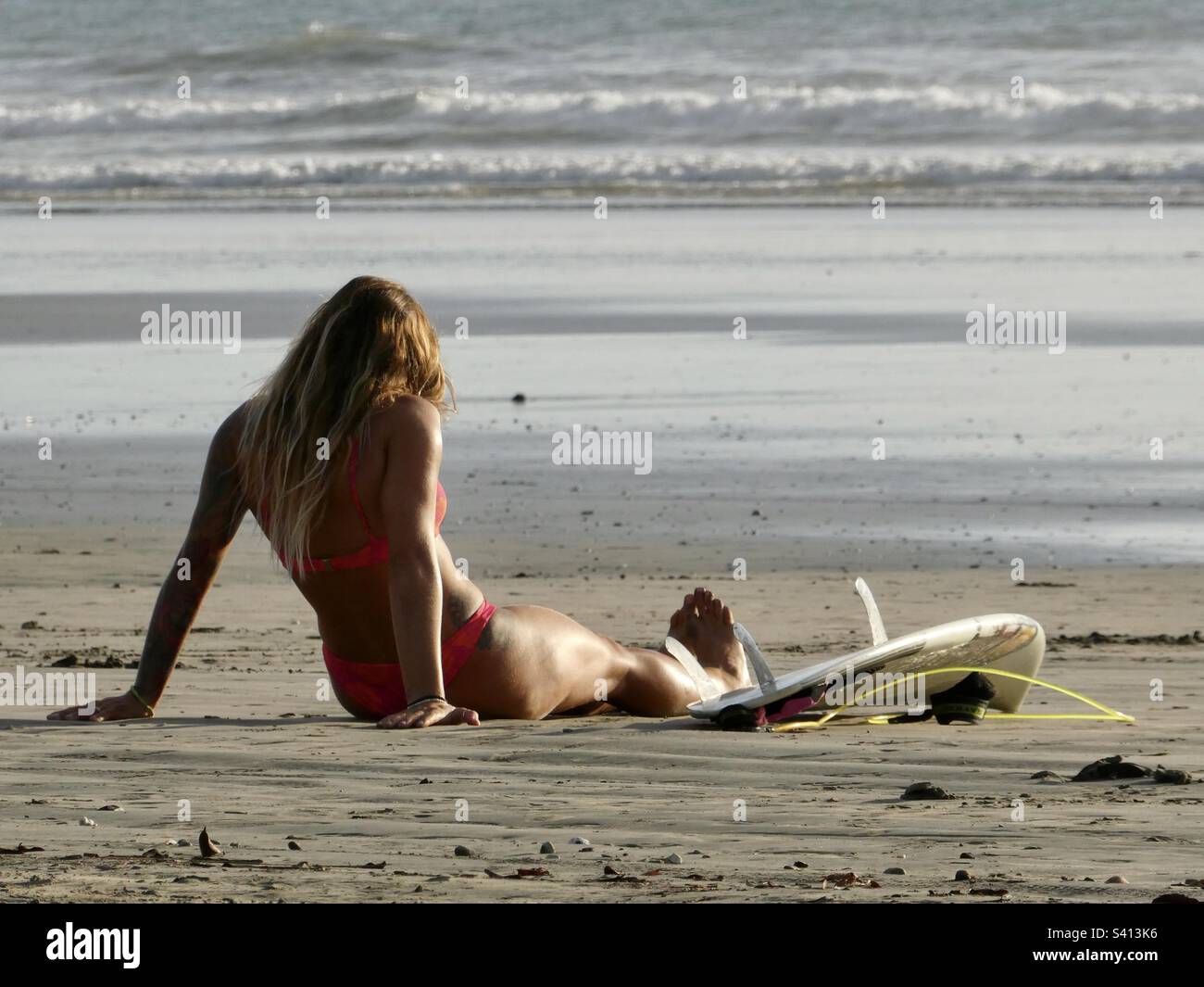 Eine Frau sitzt am Strand bei ihrem Surfbrett in Costa Rica Stockfoto