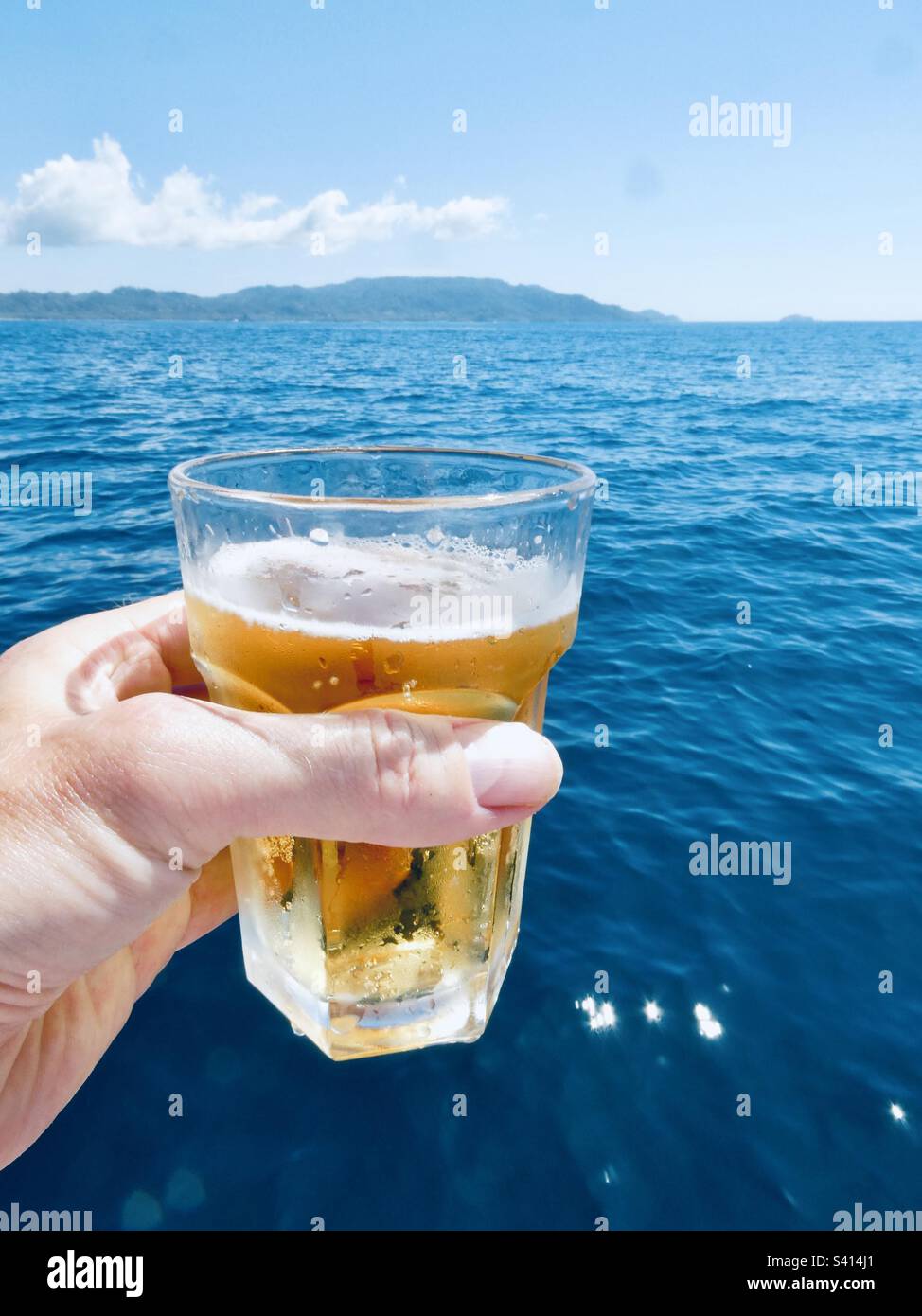 Ein Mann hält ein Glas Bier vom Deck eines Bootes auf ruhigem Wasser in Costa Rica - Smartphone-aufgenommenes Stockfoto
