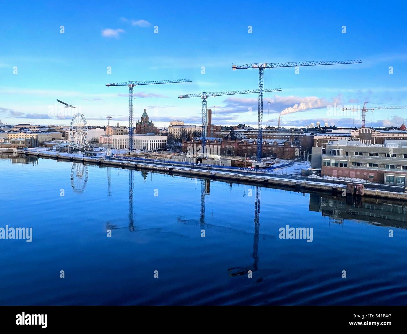 Stadthafen mit Kranen und Riesenrad, die sich im Wasser an der Küste von Helsinki spiegeln - Smartphone-aufgenommenes Stockfoto