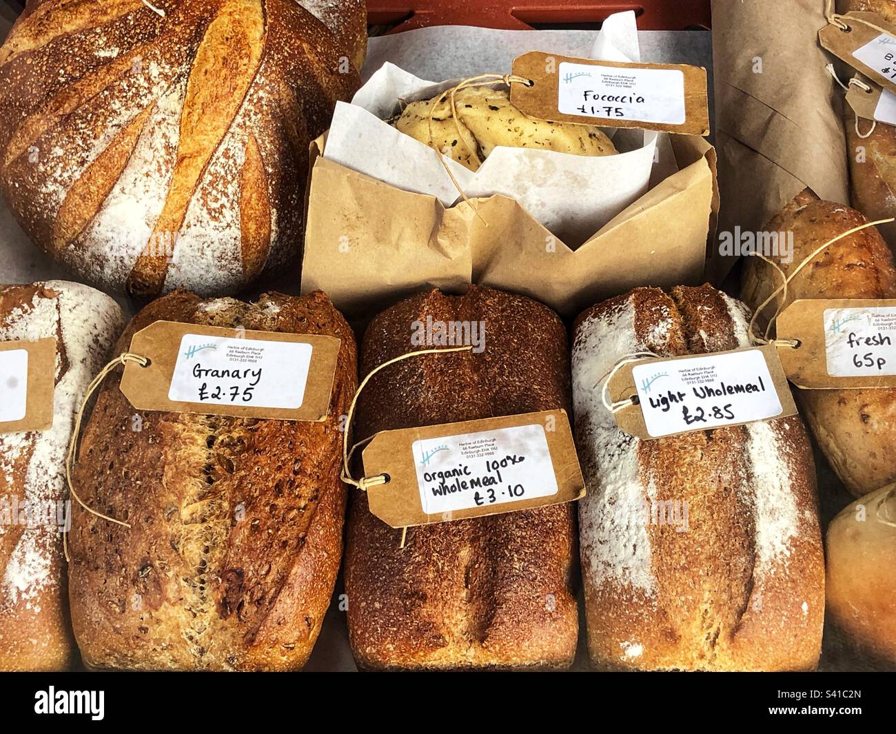 Frische hausgemachte Brotlaibe mit Preisschildern in einem Delikatessengeschäft und einer Schaufensterausstellung für Wurstwaren Stockfoto