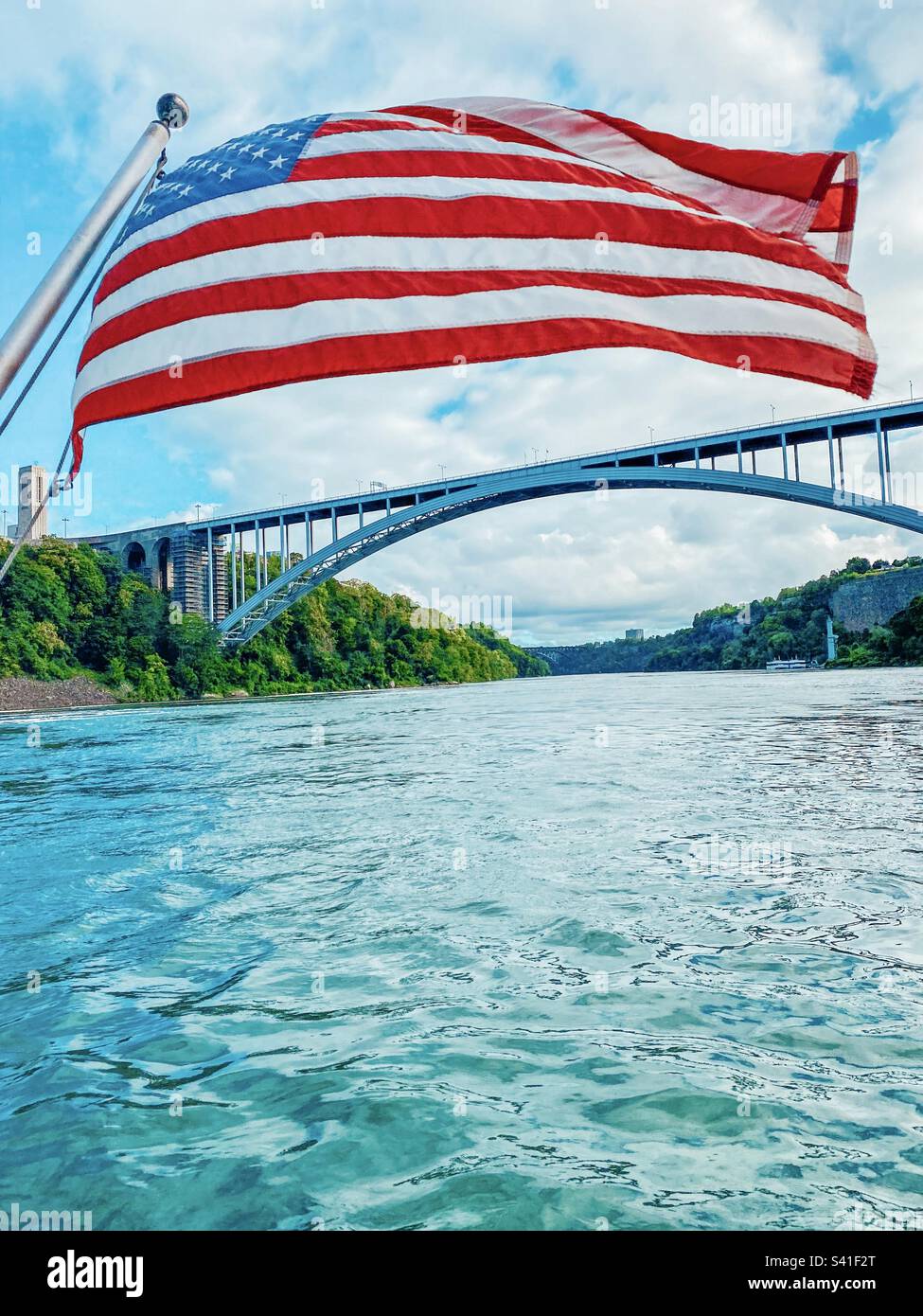 Amerikanische Flagge über dem Fluss mit Brücke im Hintergrund Stockfoto