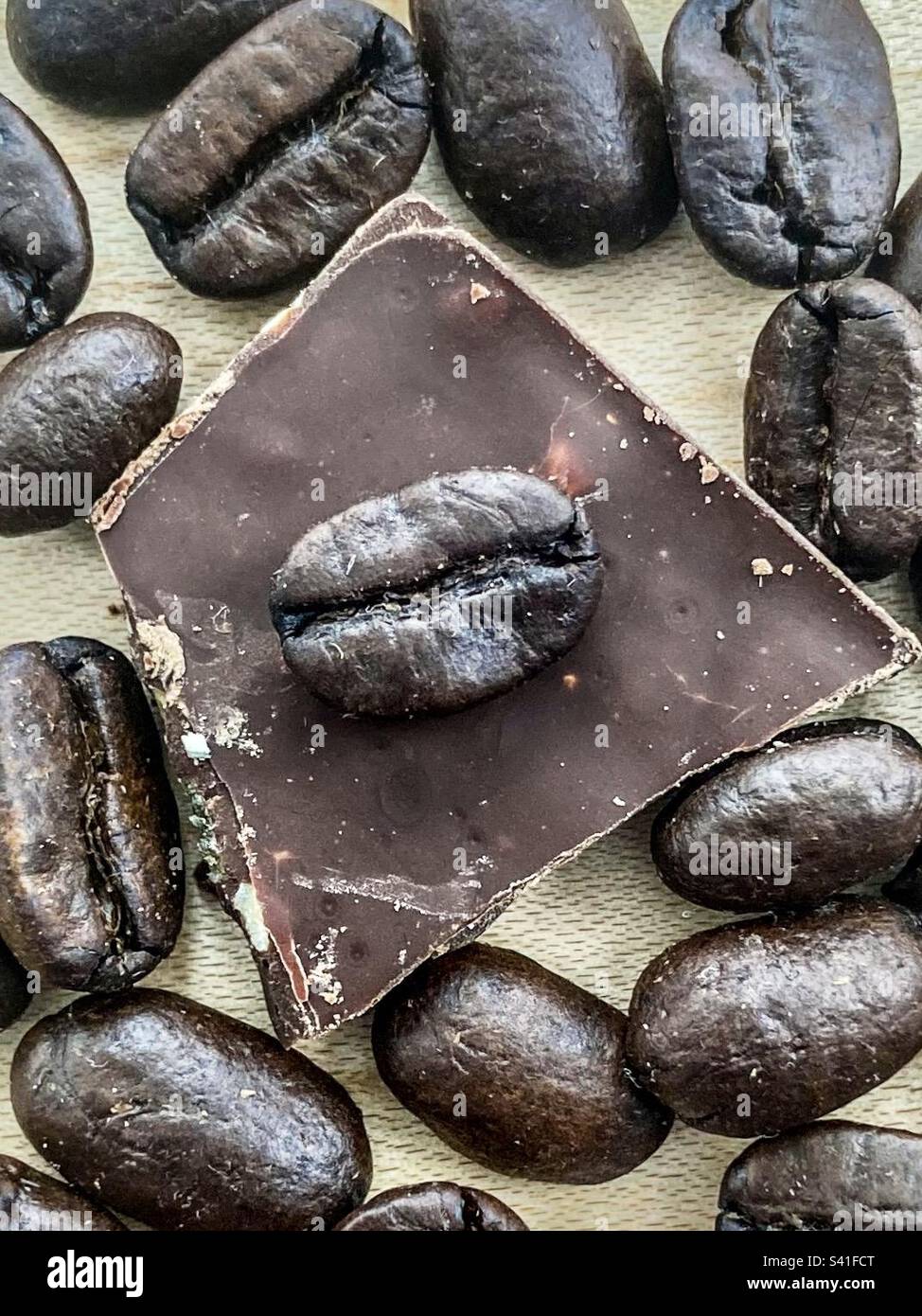 Nahaufnahme dunkel gerösteter Kaffeebohnen mit einem Stück Mandelschokolade. - Smartphone-aufgenommenes Stockfoto