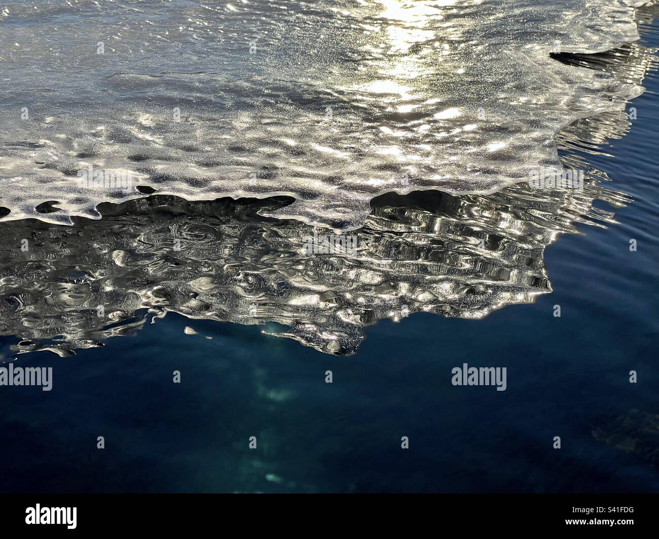 Sonnenbeleuchtete Eisdecke mit gezackter Kante, die sich im tiefblauen Wasser des Yukon River in der Nähe von Whitehorse widerspiegelt. - Smartphone-aufgenommenes Stockfoto
