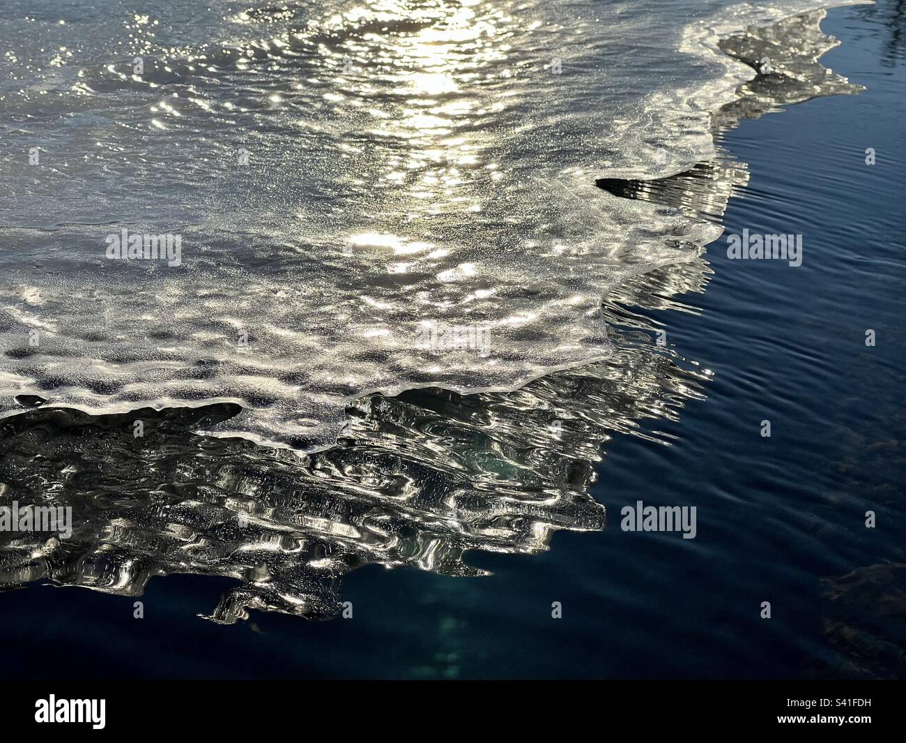 Sonnenbeleuchtete Eisdecke mit gezackter Kante, die sich im tiefblauen Wasser des Yukon River in der Nähe von Whitehorse widerspiegelt. - Smartphone-aufgenommenes Stockfoto