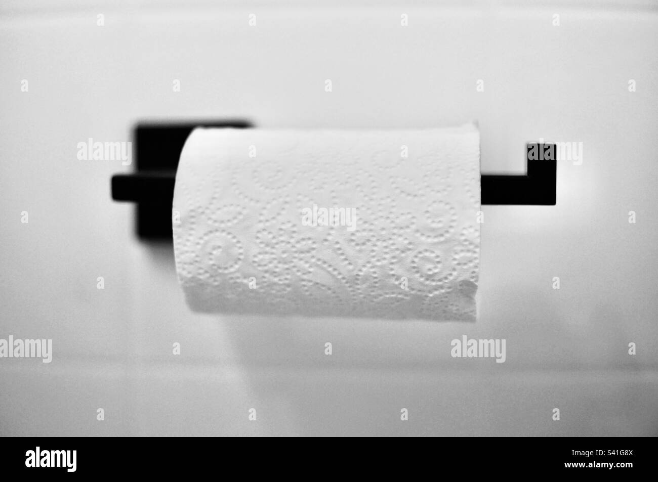 Schickes Toilettenpapier auf einem schwarzen Toilettenpapierrollenhalter. Stockfoto