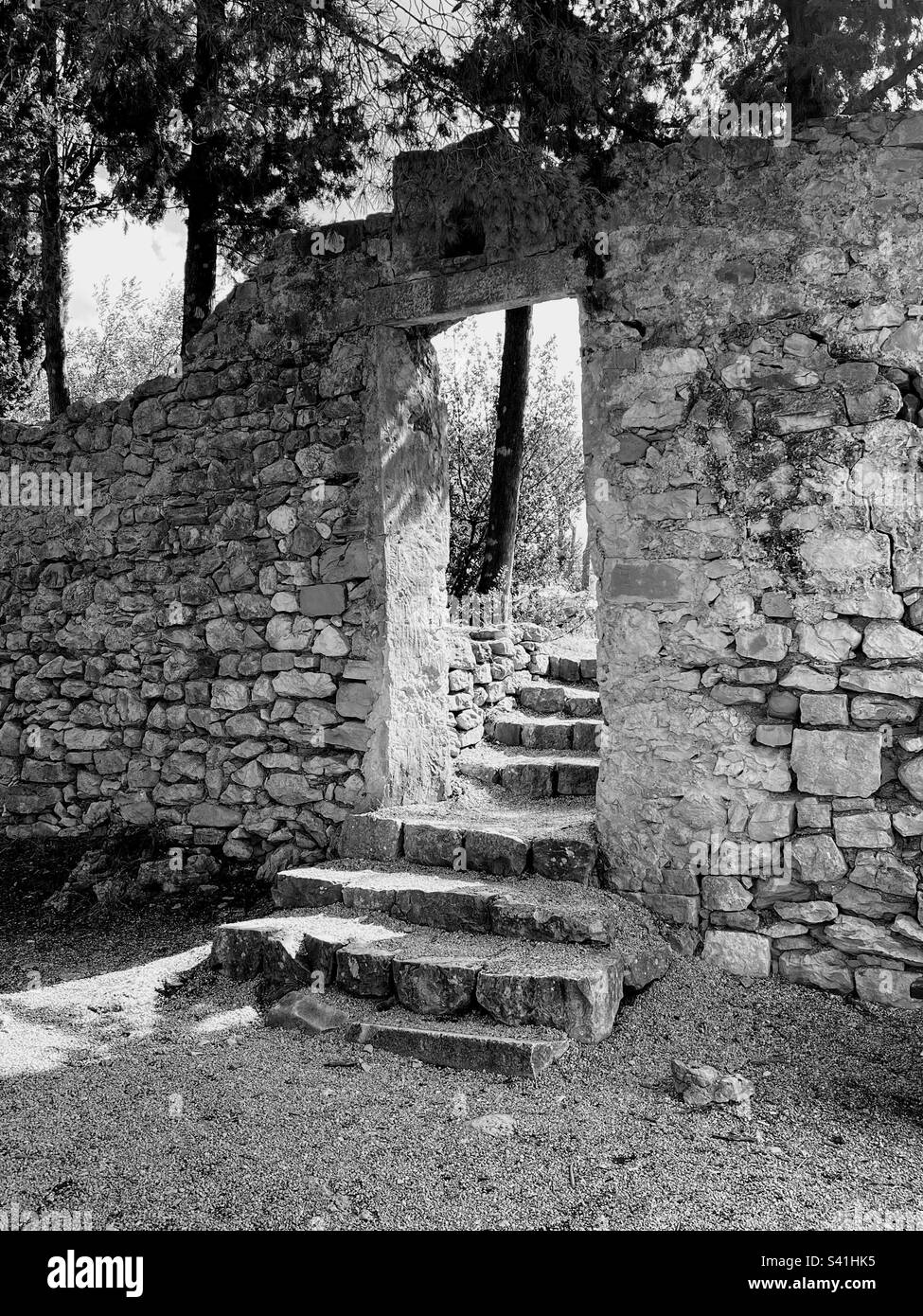 Schwarzweiß-Monochrom-Seitenansicht der verfallenen alten Sandsteinwand mit Bogen und Treppe in der Mitte - Smartphone-aufgenommenes Stockfoto