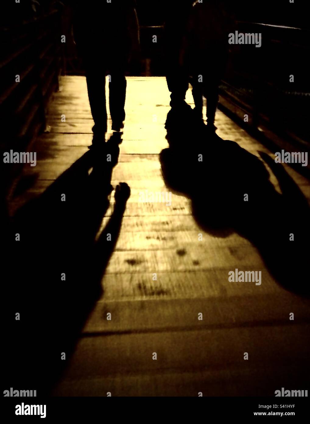 Silhouette der Beine von zwei Personen, die nachts im Dunkeln gehen, mit einem gelben Licht im Hintergrund Stockfoto