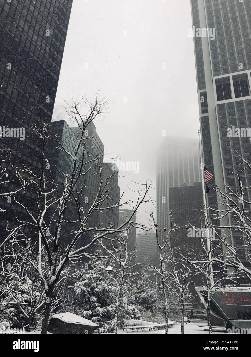 Schnee bedeckt Gebäude, Seitenstraßen und Bäume im Financial District, Manhattan, USA und USA Flagge. Verschneiter und nebiger Tag in Manhattan Stockfoto