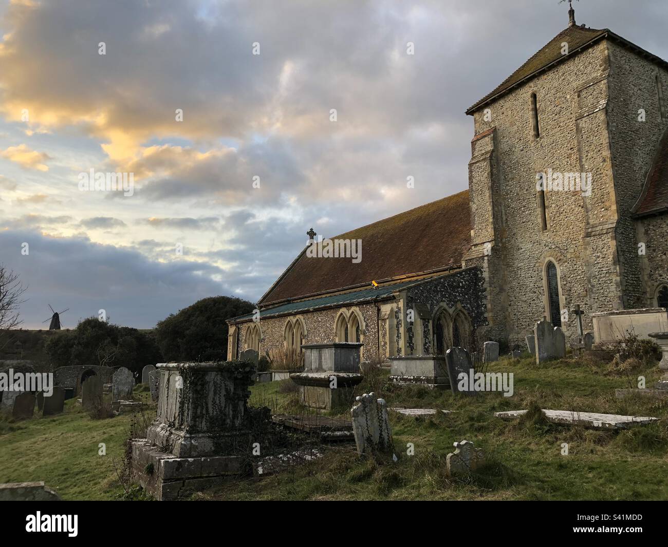 St. Margaret's Church mit Beacon Mill auf dem Hügel im Hintergrund in Rottingdean, East Sussex, England. - Smartphone-aufgenommenes Stockfoto