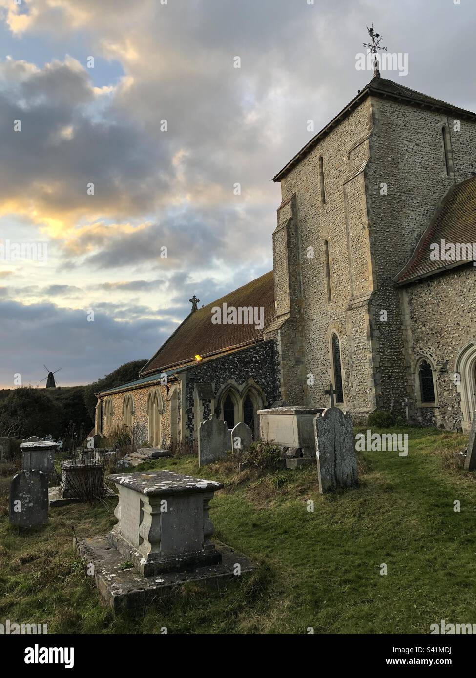 St. Margaret's Church mit Beacon Mill auf dem Hügel im Hintergrund in Rottingdean, West Sussex, England. - Smartphone-aufgenommenes Stockfoto