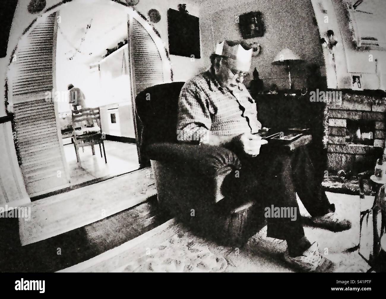 Ein Mann mit Weihnachtsmütze sitzt auf einem Stuhl und schaut sich ein Geschenk an - Smartphone-aufgenommenes Stockfoto