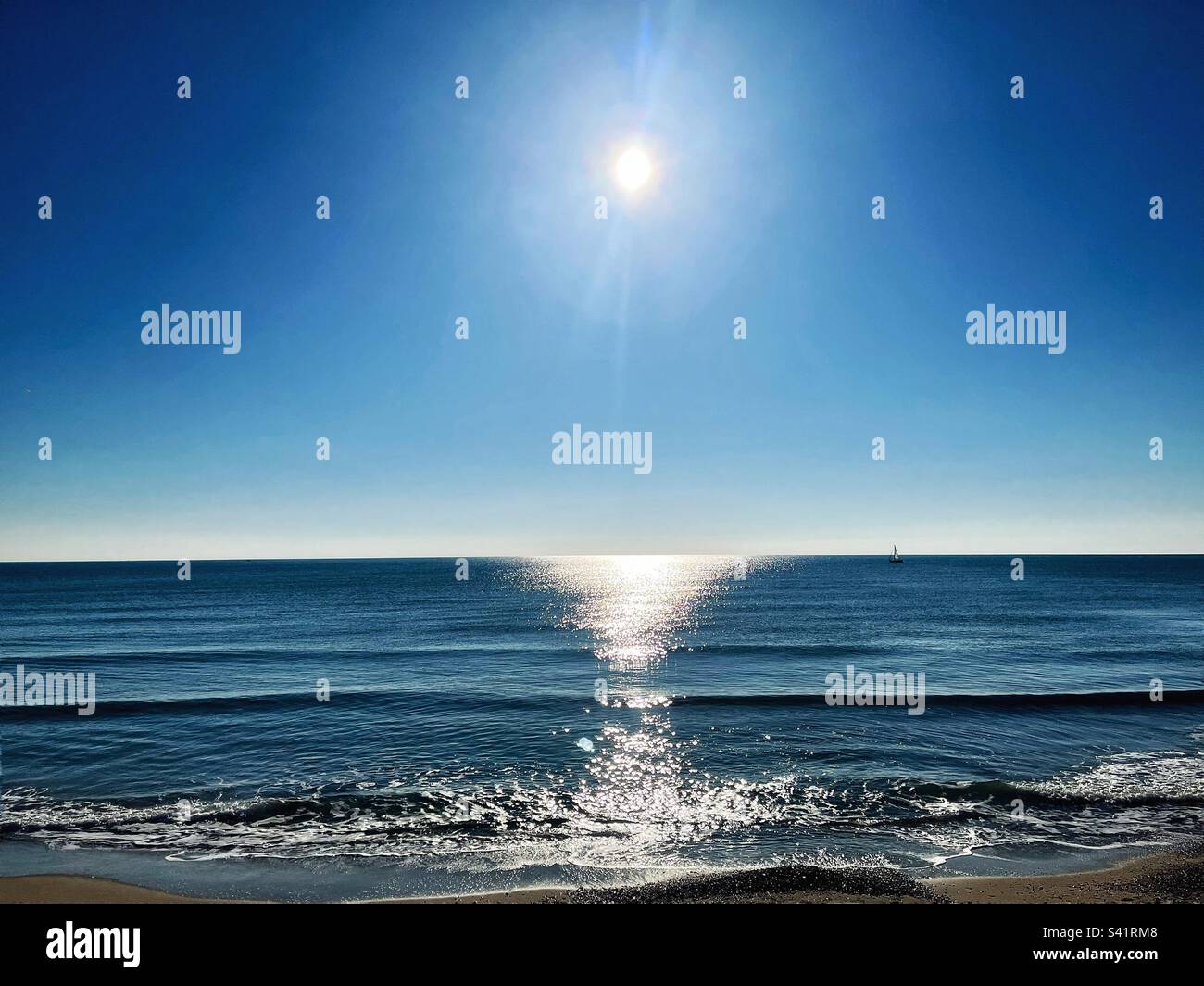Sonnenreflexionen auf dem Meer, während die Wellen am Strand Wellen und Runden schlagen. Horizont und schimmerndes Licht. Mittelmeer. - Smartphone-aufgenommenes Stockfoto
