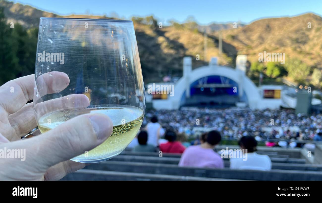 LOS ANGELES, CA, AUGUST 2022: Konzentrieren Sie sich auf die Hand, indem Sie ein Plastikglas mit Weißwein halten, mit einem sanften Fokus auf das Publikum beim Hollywood Bowl vor einem Konzert im Hintergrund Stockfoto