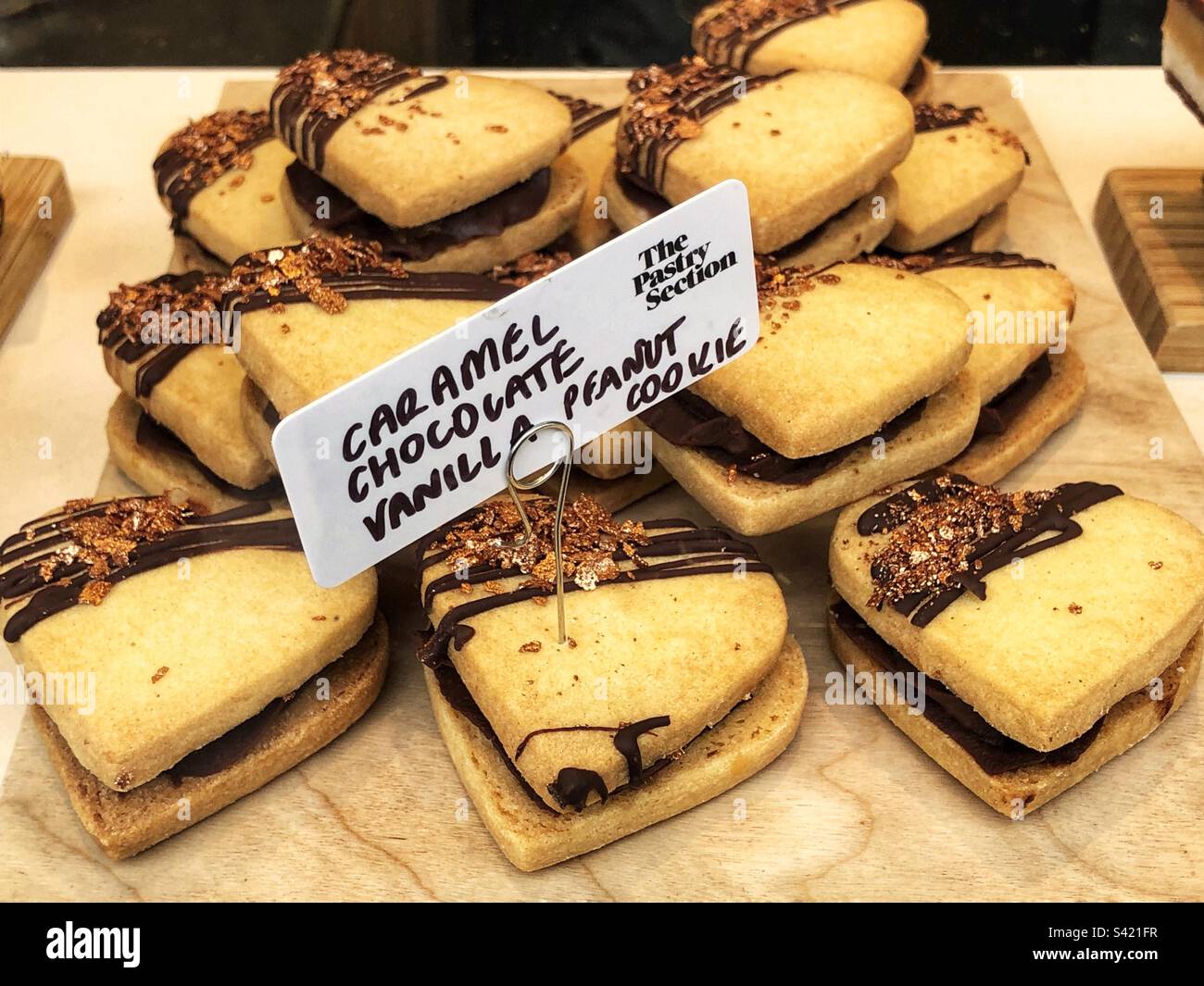 Herzförmiger Karamellschokolade-Vanille-Erdnuss-Keks im Fenster des Bäckereigeschäfts - Smartphone-aufgenommenes Stockfoto
